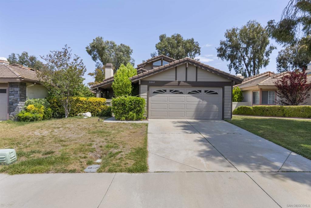 Single-story home with a gray double garage, broad concrete driveway, and landscaped front yard.