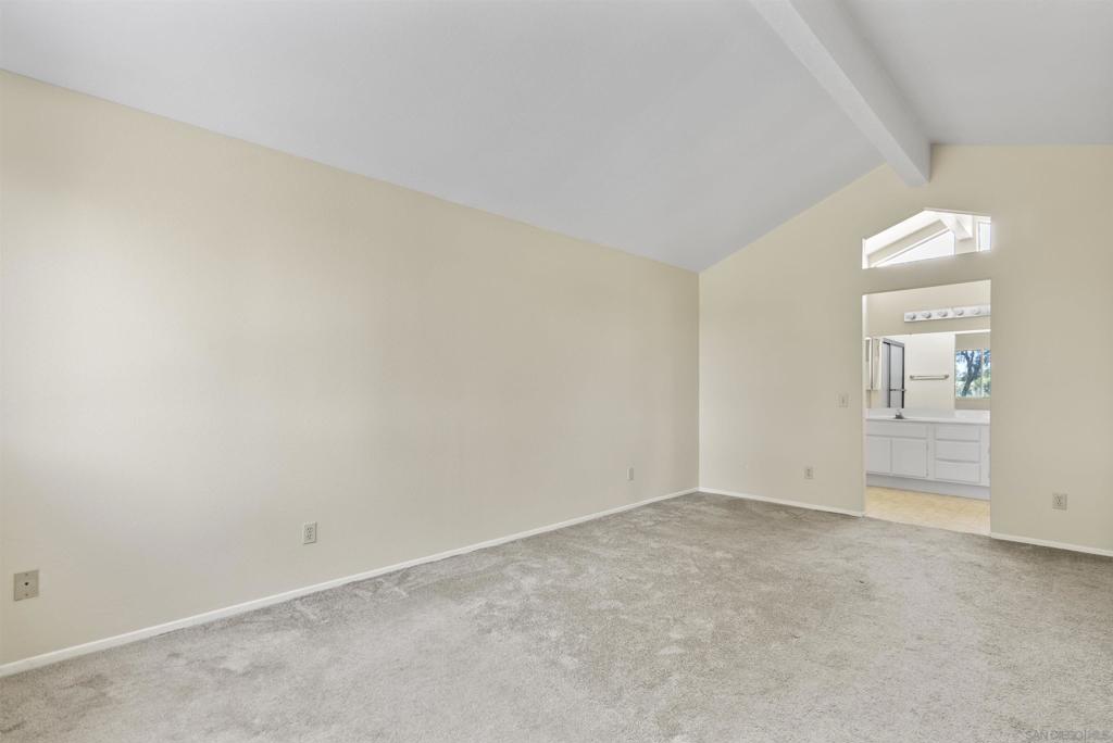 Empty carpeted room with a vaulted ceiling and an open doorway to a bathroom.