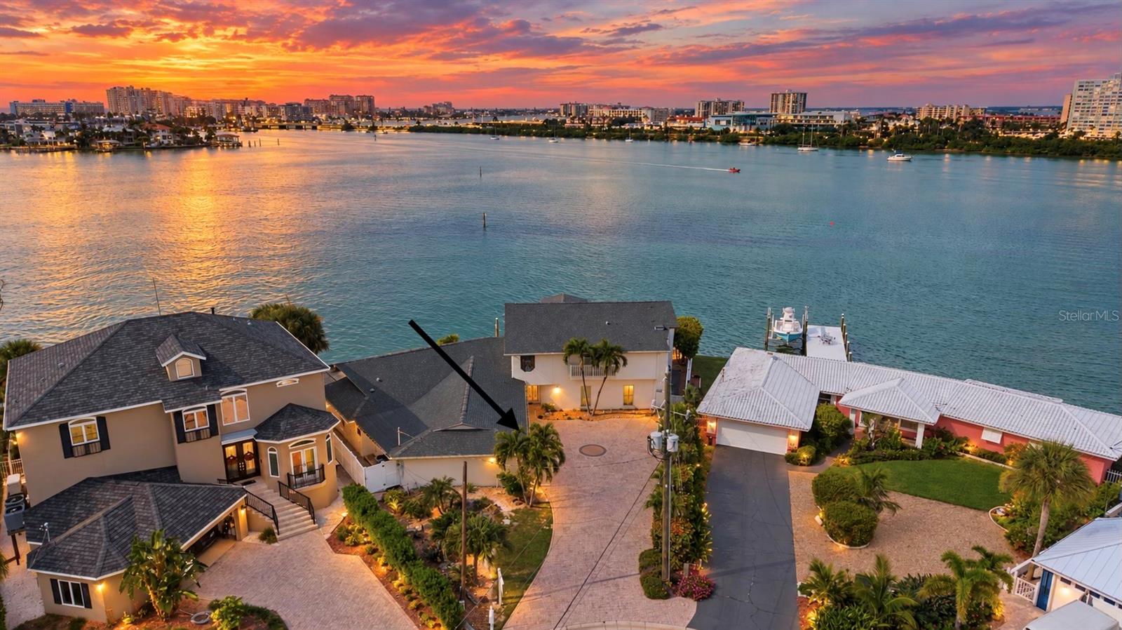 Waterfront home indicated by an arrow, with bay, docks, and sunset skyline.