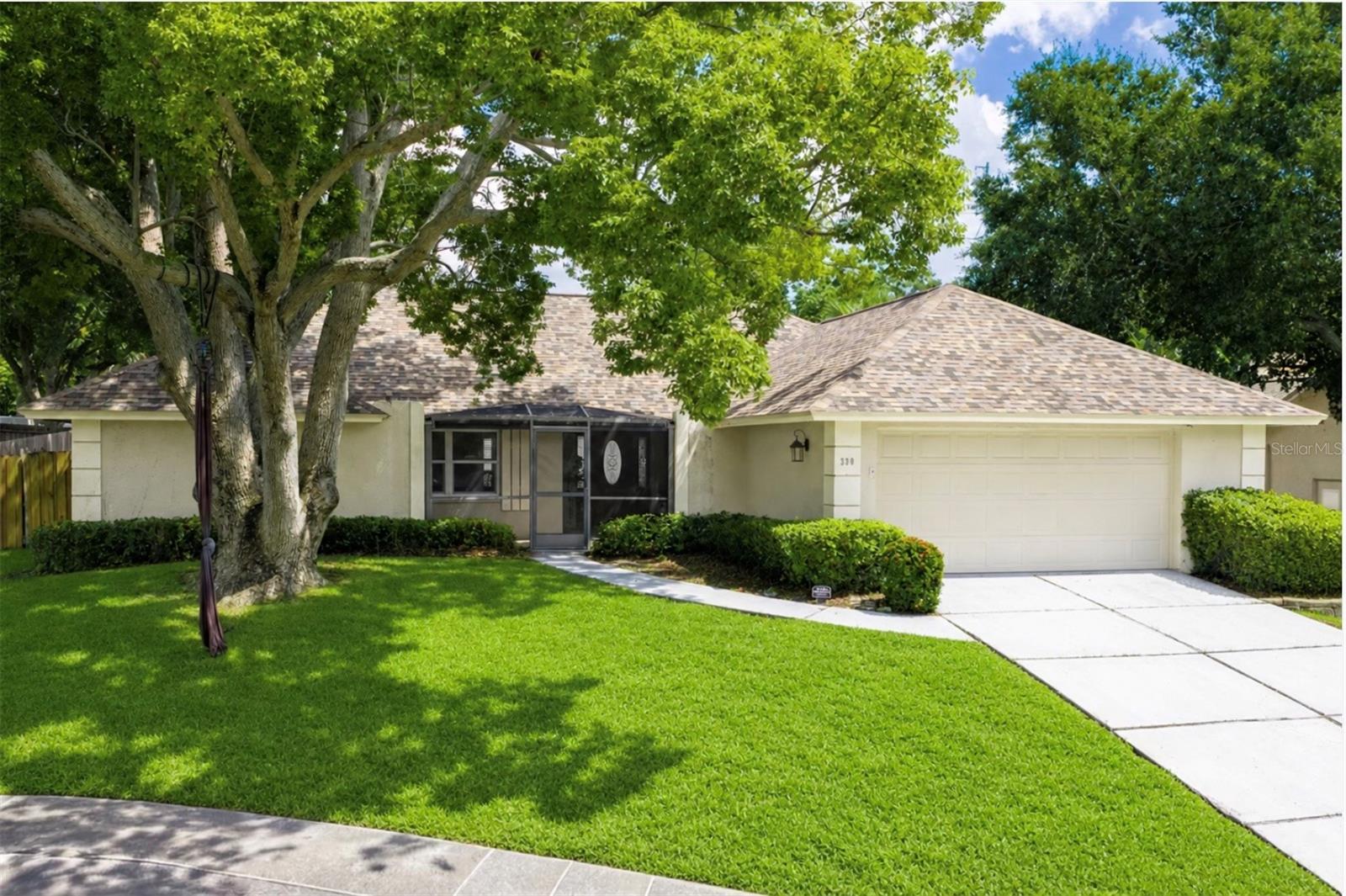 Single-story home with a two-car garage, screened entry, and mature trees shading the front lawn.