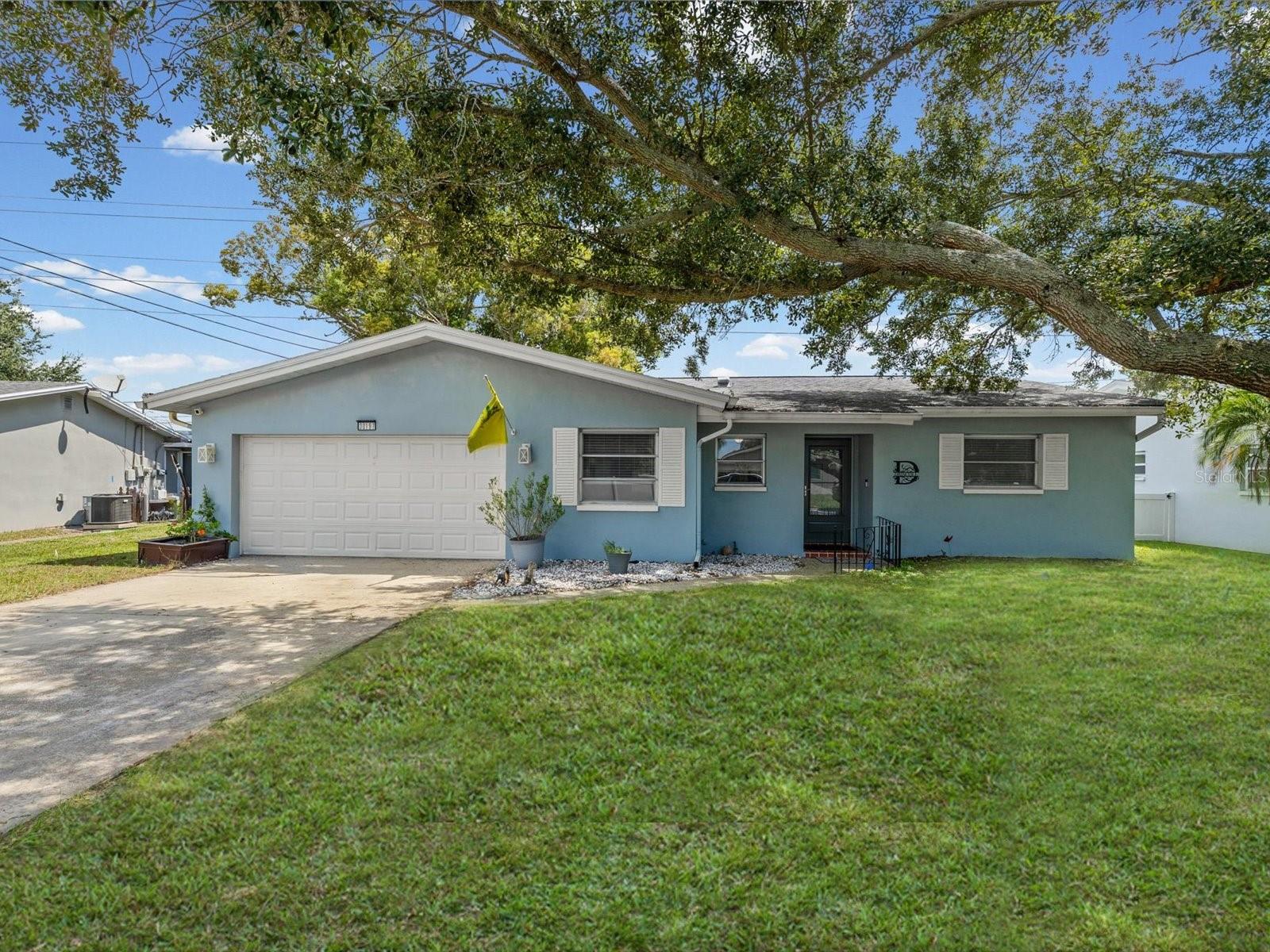 Blue single-story house with an attached double garage beneath a sprawling oak tree.