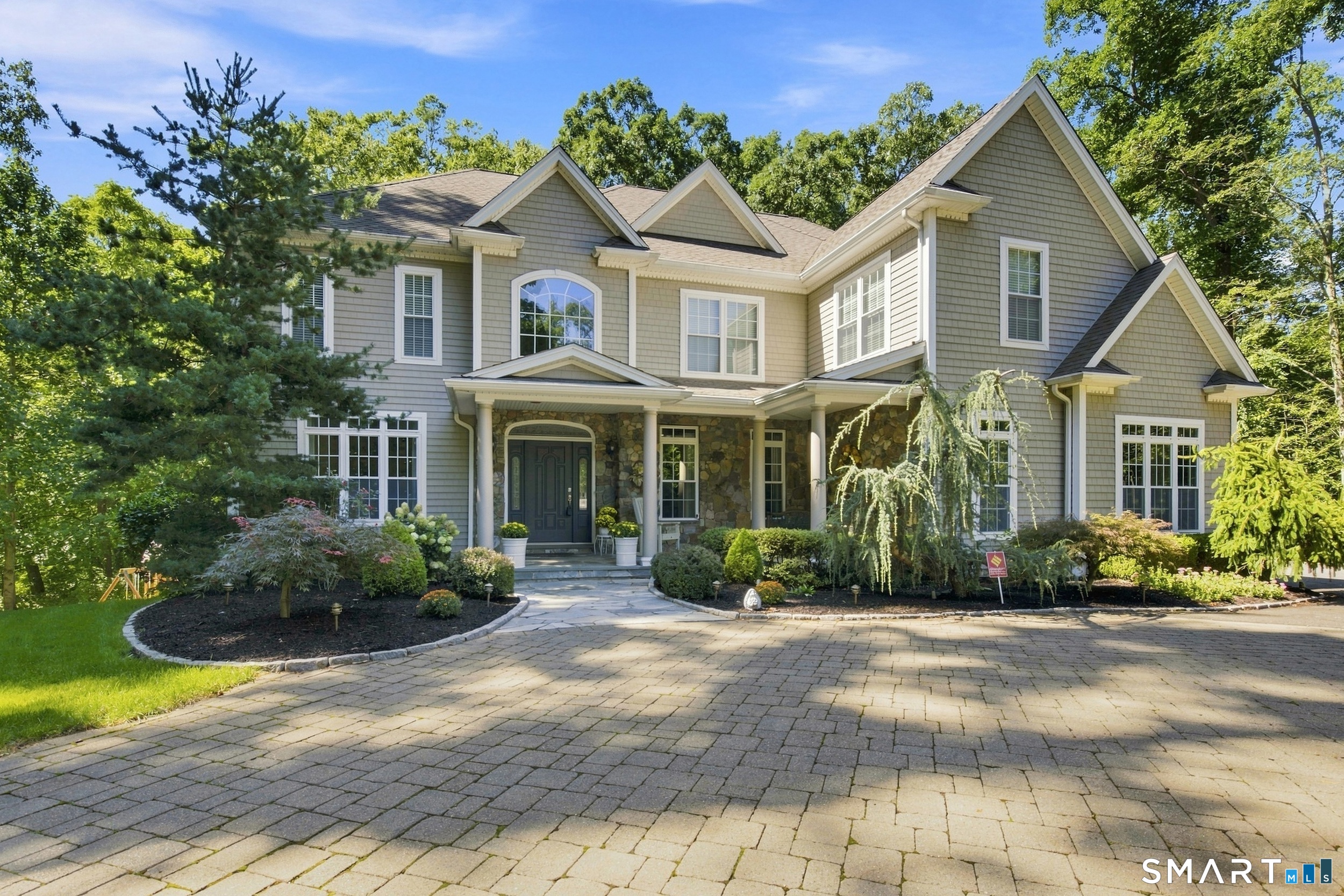 Gray multi-gabled home with a stone entry, landscaped gardens, and a broad paved driveway.