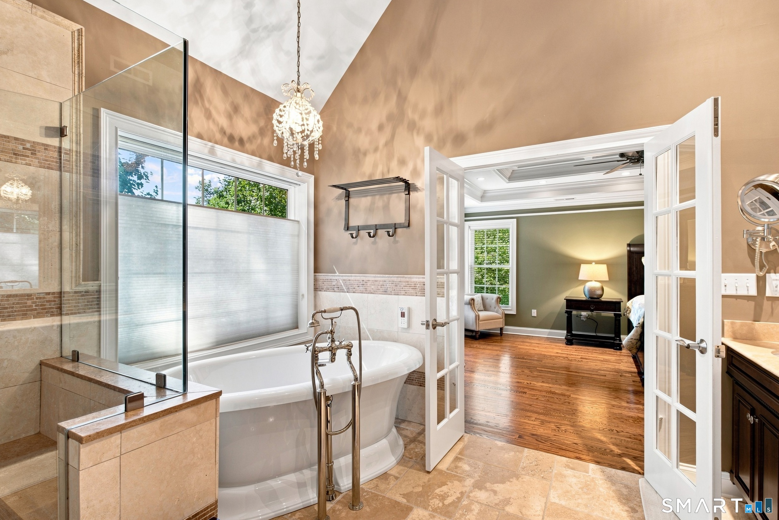 Bathroom with a freestanding soaking tub and glass shower, opening to a furnished sitting room.