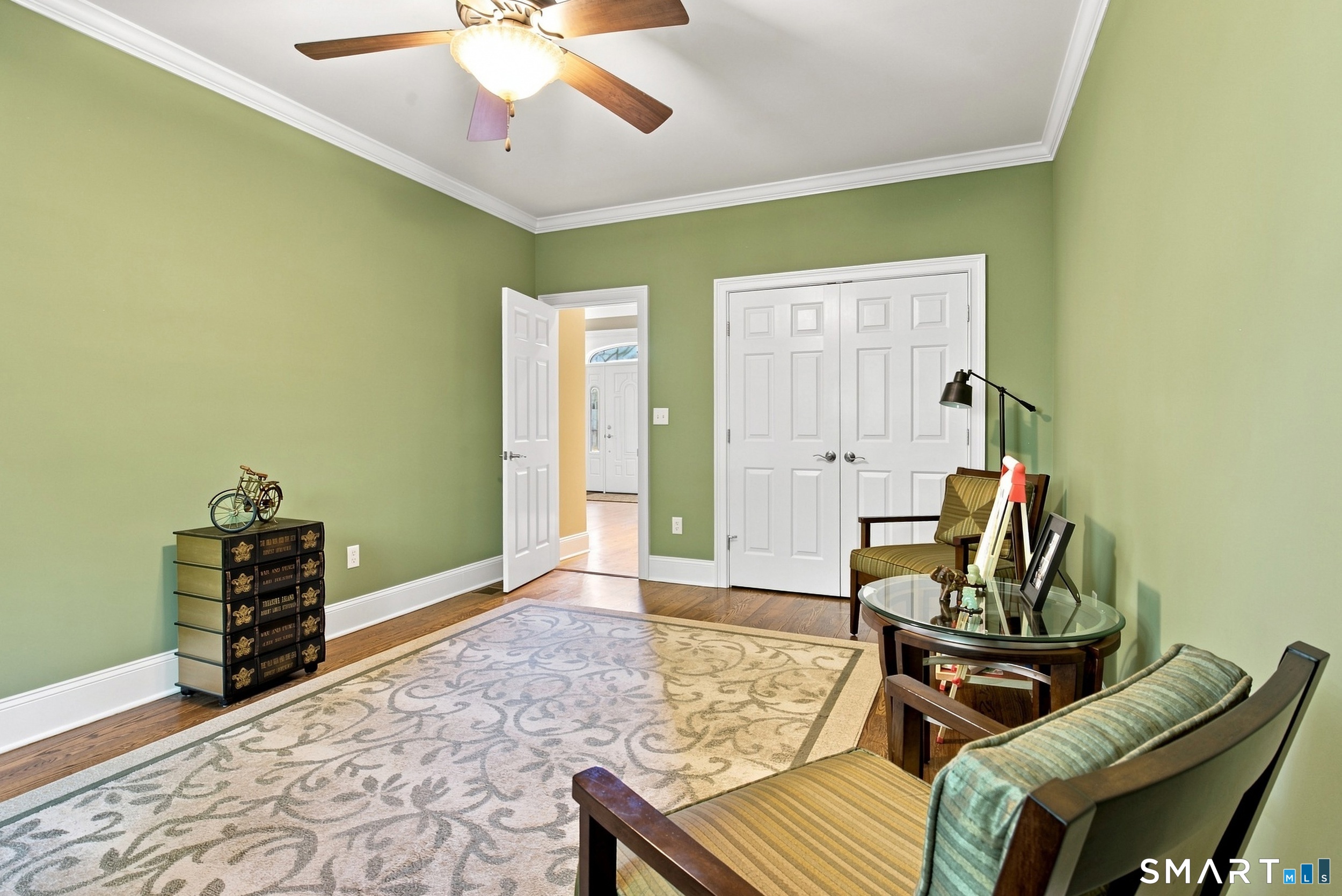 Furnished sitting room with sage-green walls, a patterned rug, and a ceiling fan.