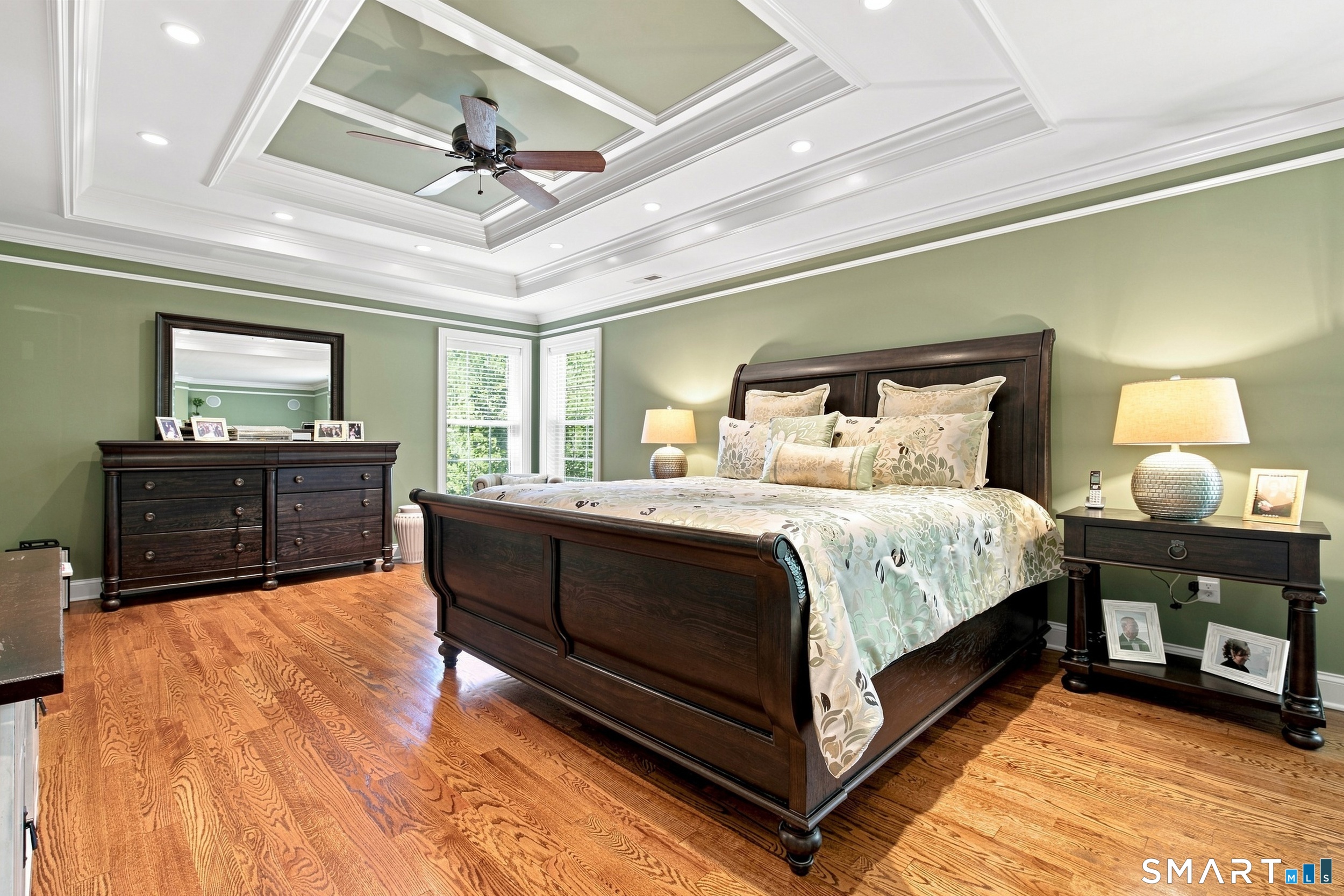 Bedroom with a dark wood bed, sage green walls, hardwood floors, and a detailed coffered ceiling.