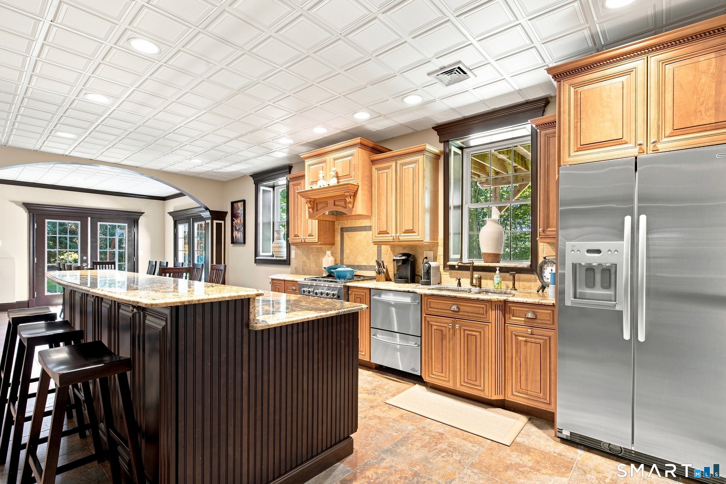 Spacious kitchen with a granite island, warm wood cabinets, stainless appliances, and a coffered ceiling.