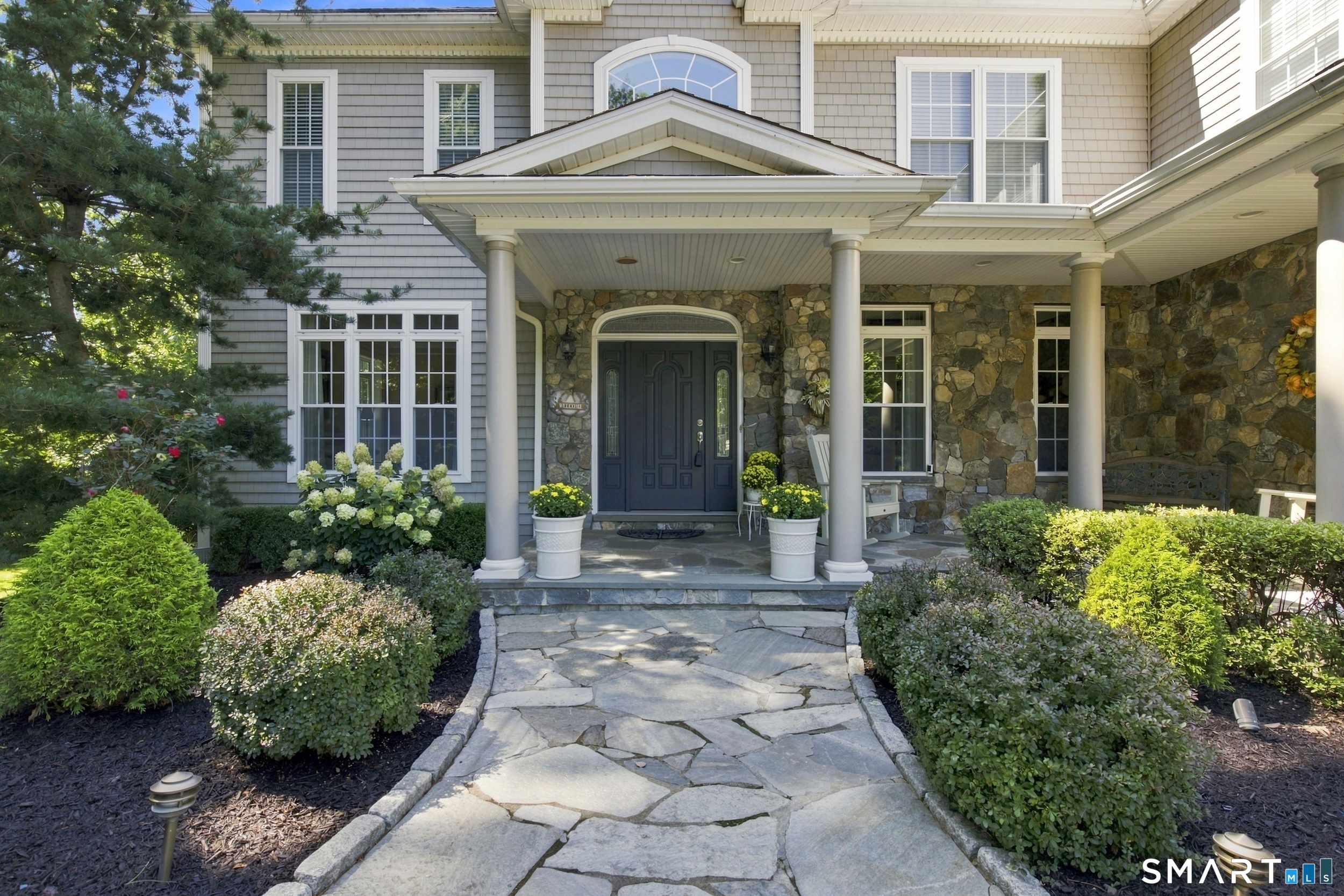 House entrance with a stone facade, columned covered porch, and landscaped flagstone walkway.