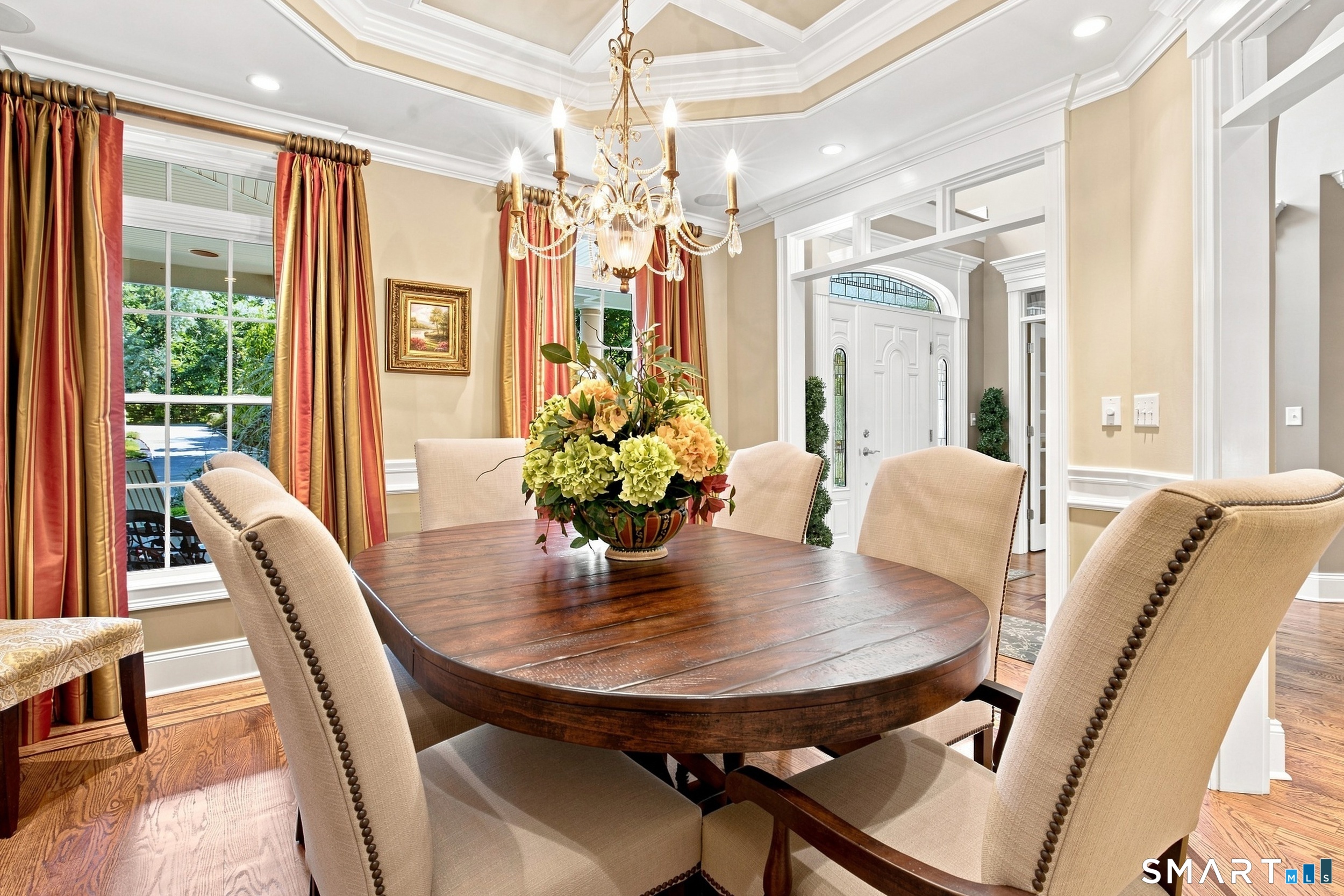 Dining room with an oval wood table, cream chairs, floral centerpiece, and ornate chandelier.