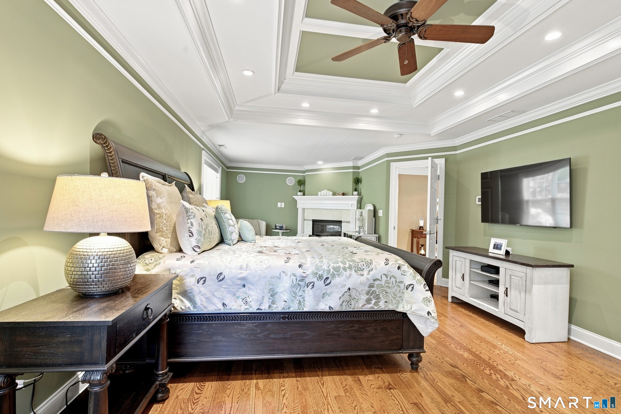 Bedroom with sage-green walls, a tray ceiling, dark wood bed, and fireplace.