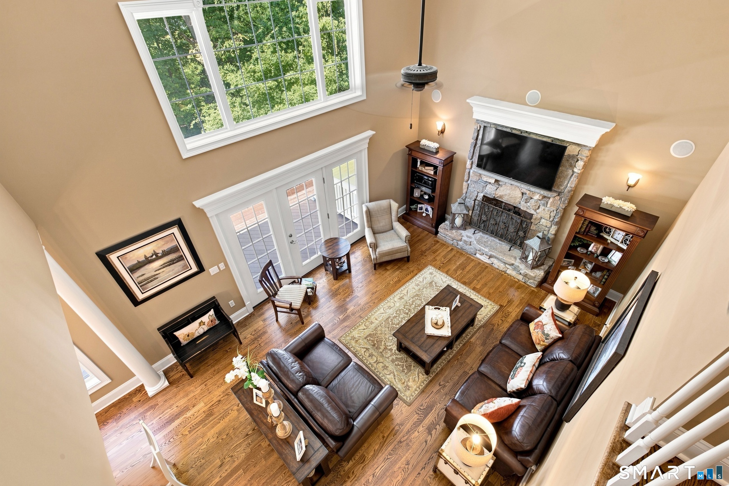 Vaulted living room with leather sofas, hardwood floors, a large window, and a stone fireplace.