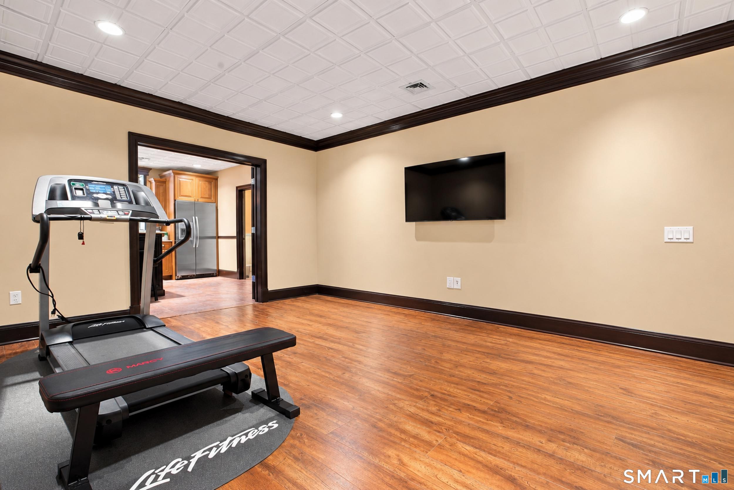 Home gym with treadmill, exercise bench, wall-mounted television, and hardwood floors.