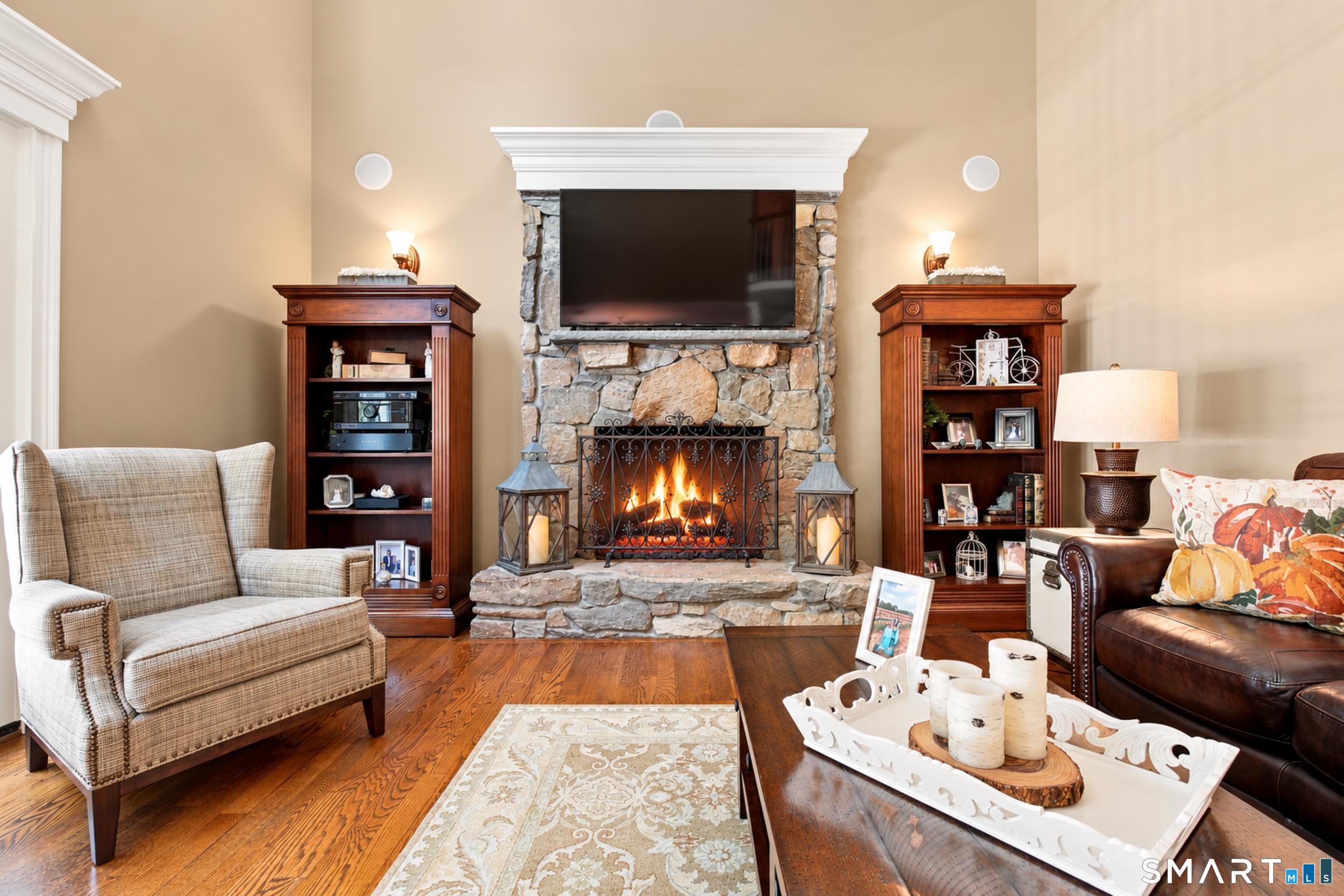 Living room with a stone fireplace, mounted television, wood bookcases, and hardwood floors.