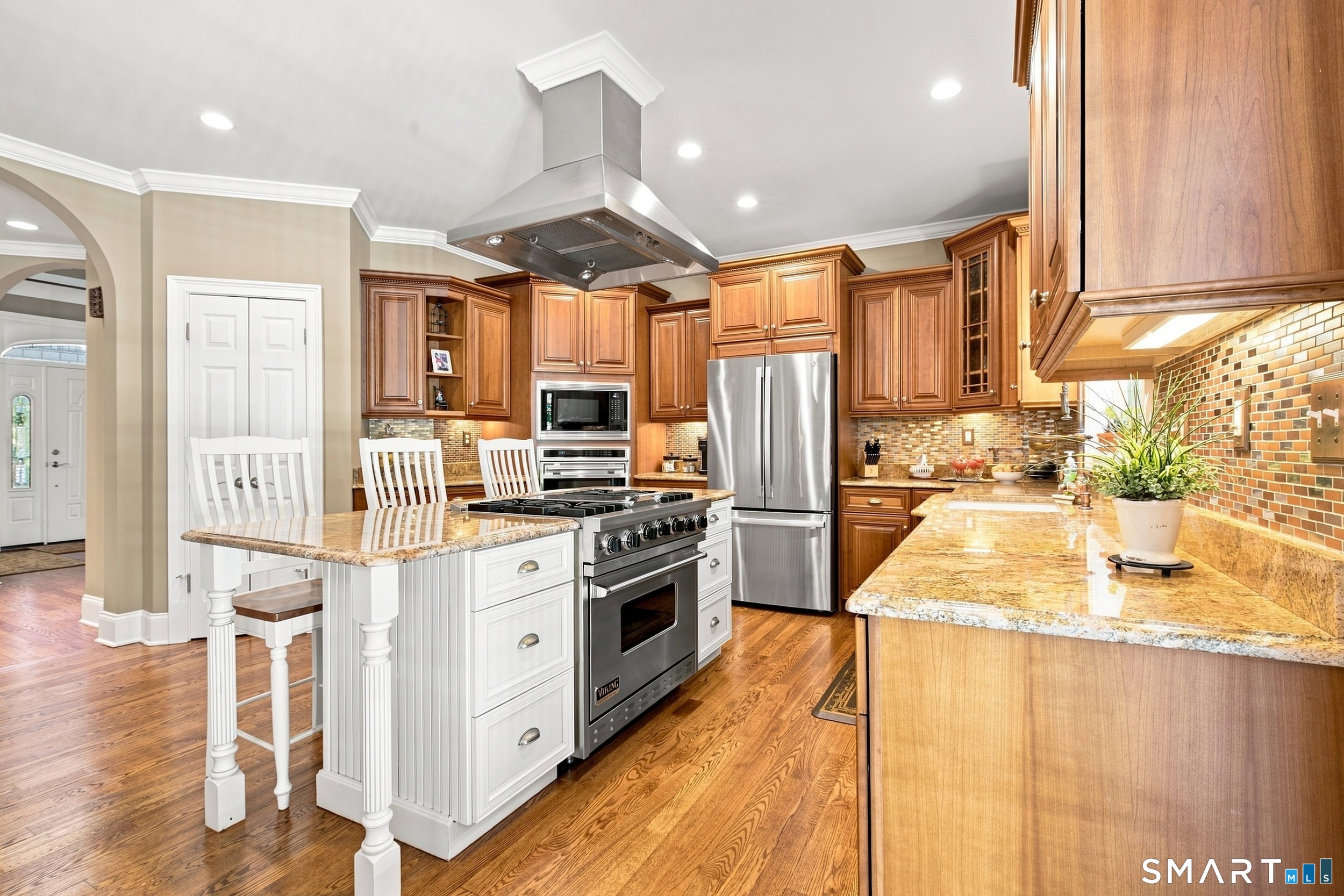 Kitchen with warm wood cabinets, granite counters, stainless appliances, and a white island with a range.