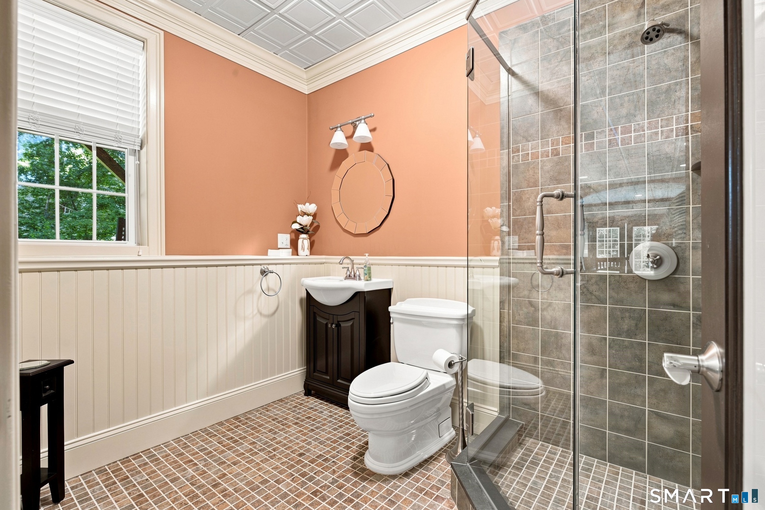 Bathroom with peach walls, beadboard wainscoting, and a glass-enclosed tiled shower.