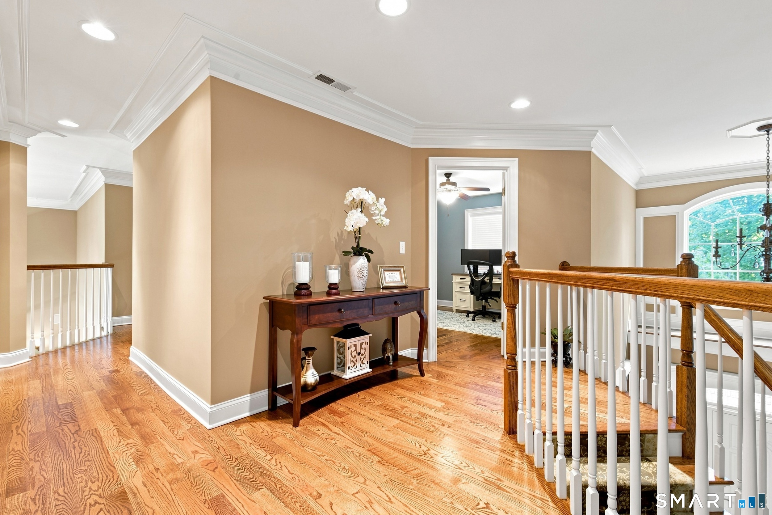 Upstairs landing with hardwood floors, white balusters, and a console table beside an office doorway.