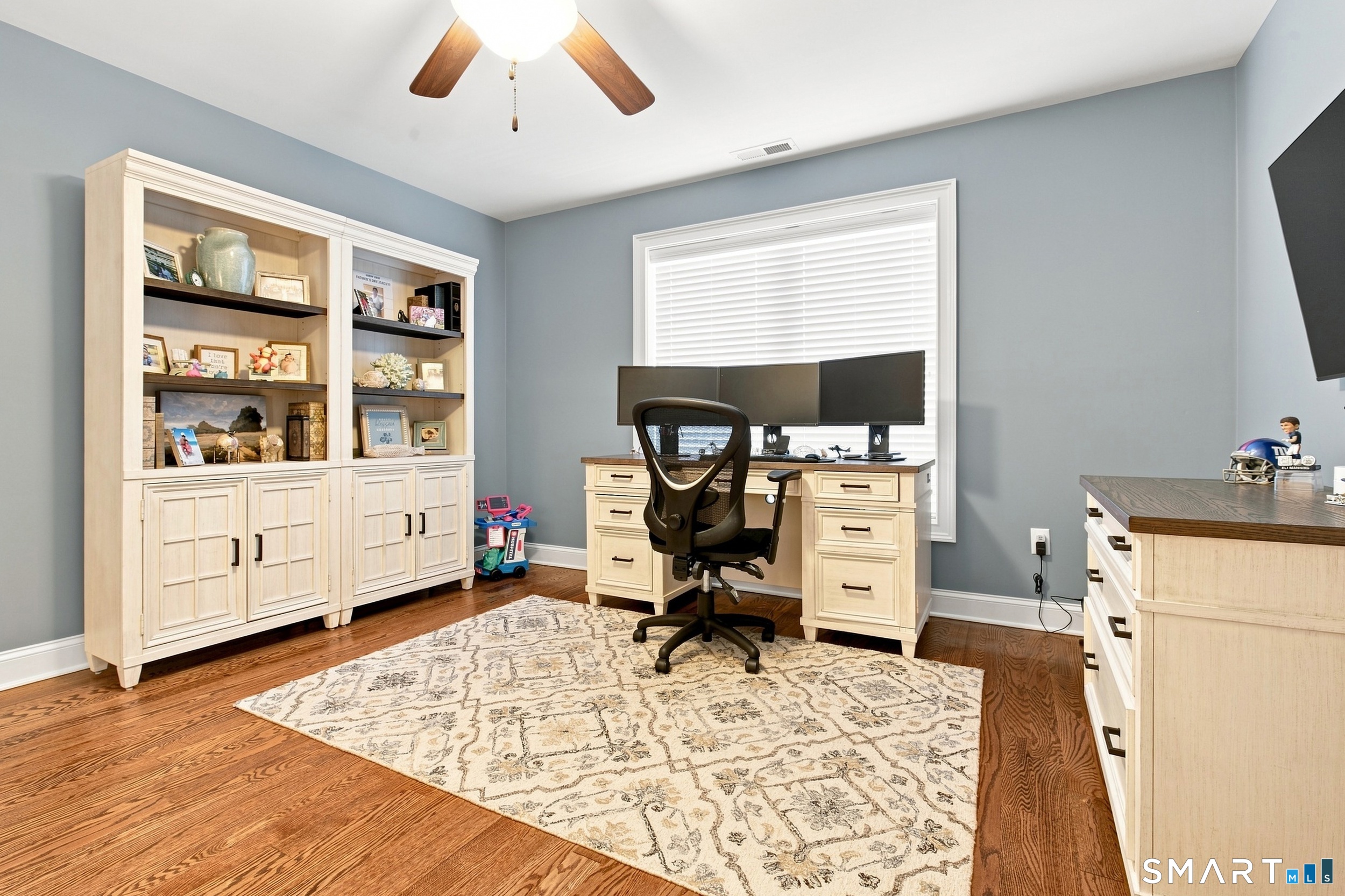 Home office with built-in cream cabinetry, a three-monitor desk, and hardwood floors.