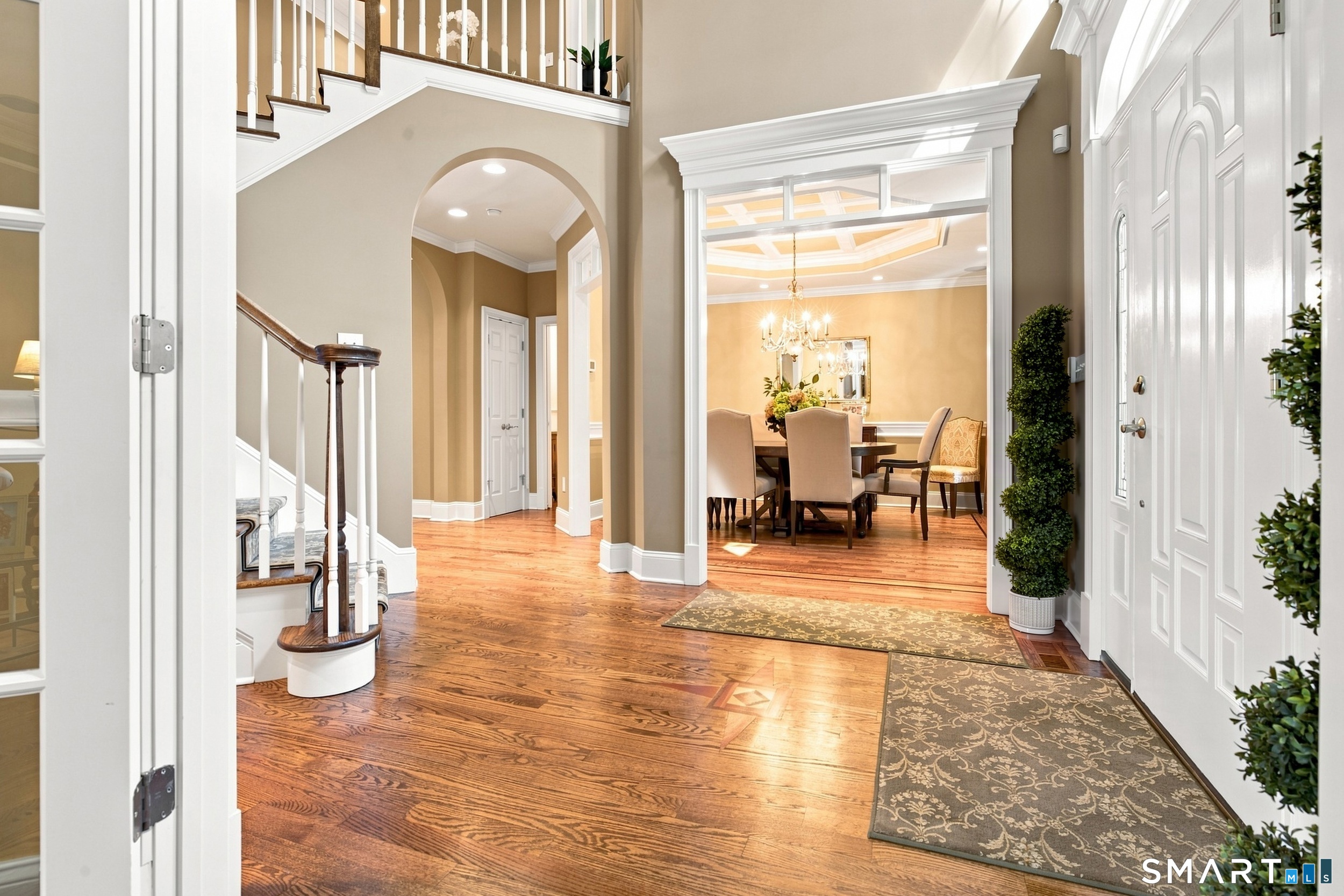 Grand foyer with curved staircase, hardwood floors, and dining room beyond.