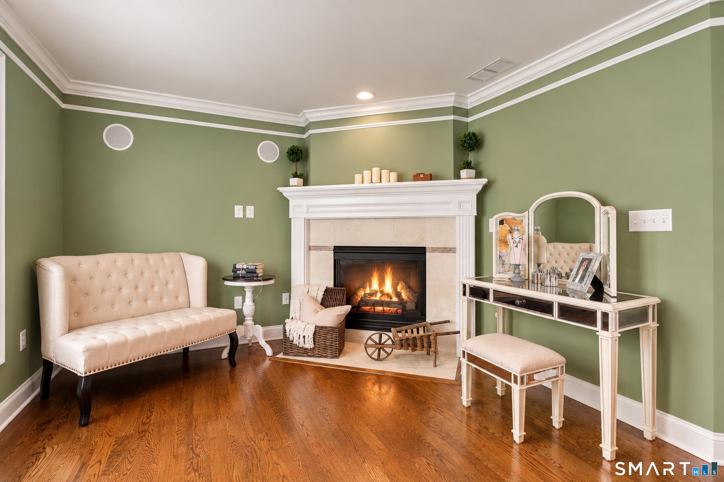 Living room with a lit fireplace, sage-green walls, dark hardwood floors, and cream furniture.