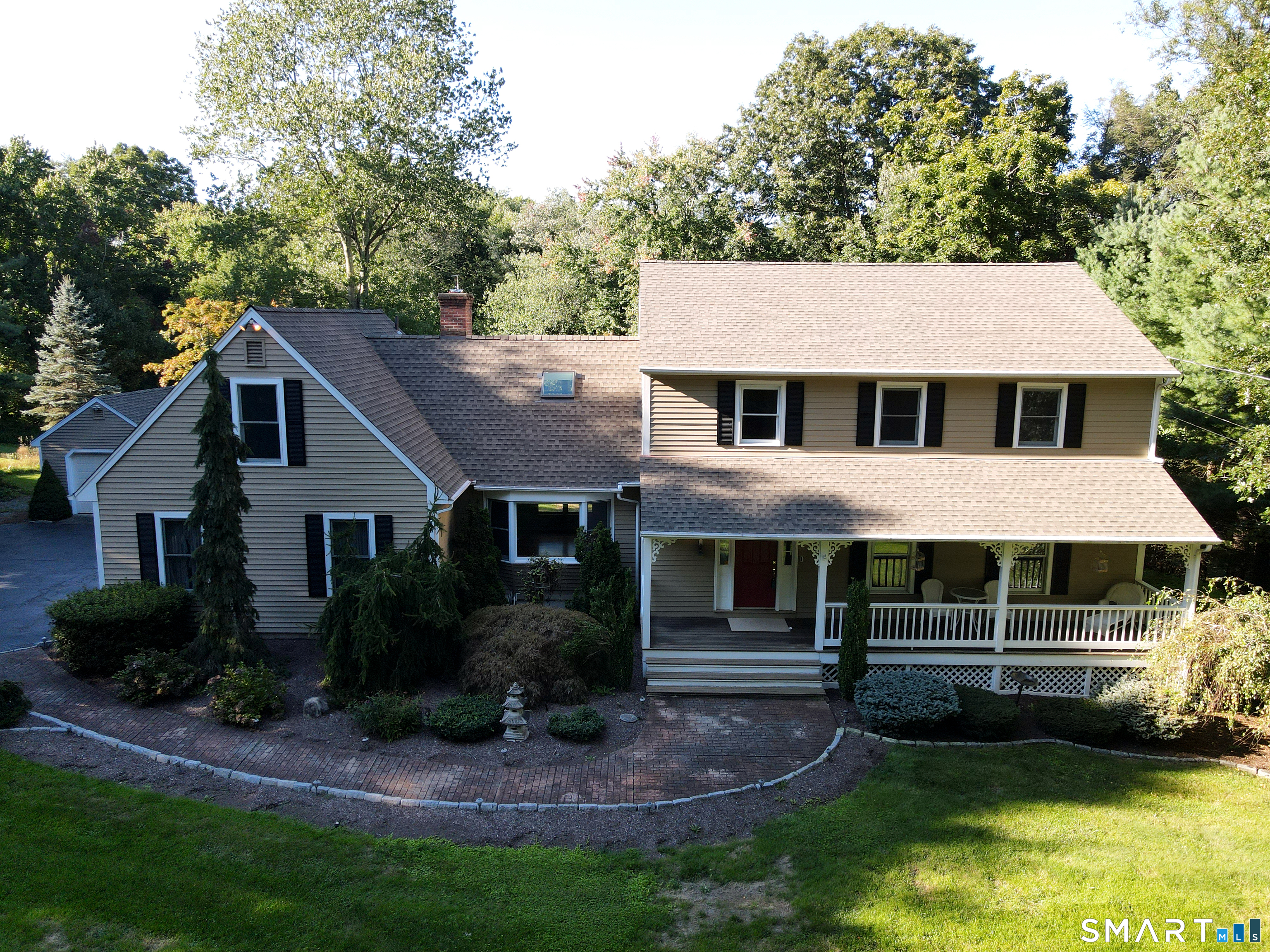 Gray-sided house with a covered porch, curved brick walkway, and mature trees.