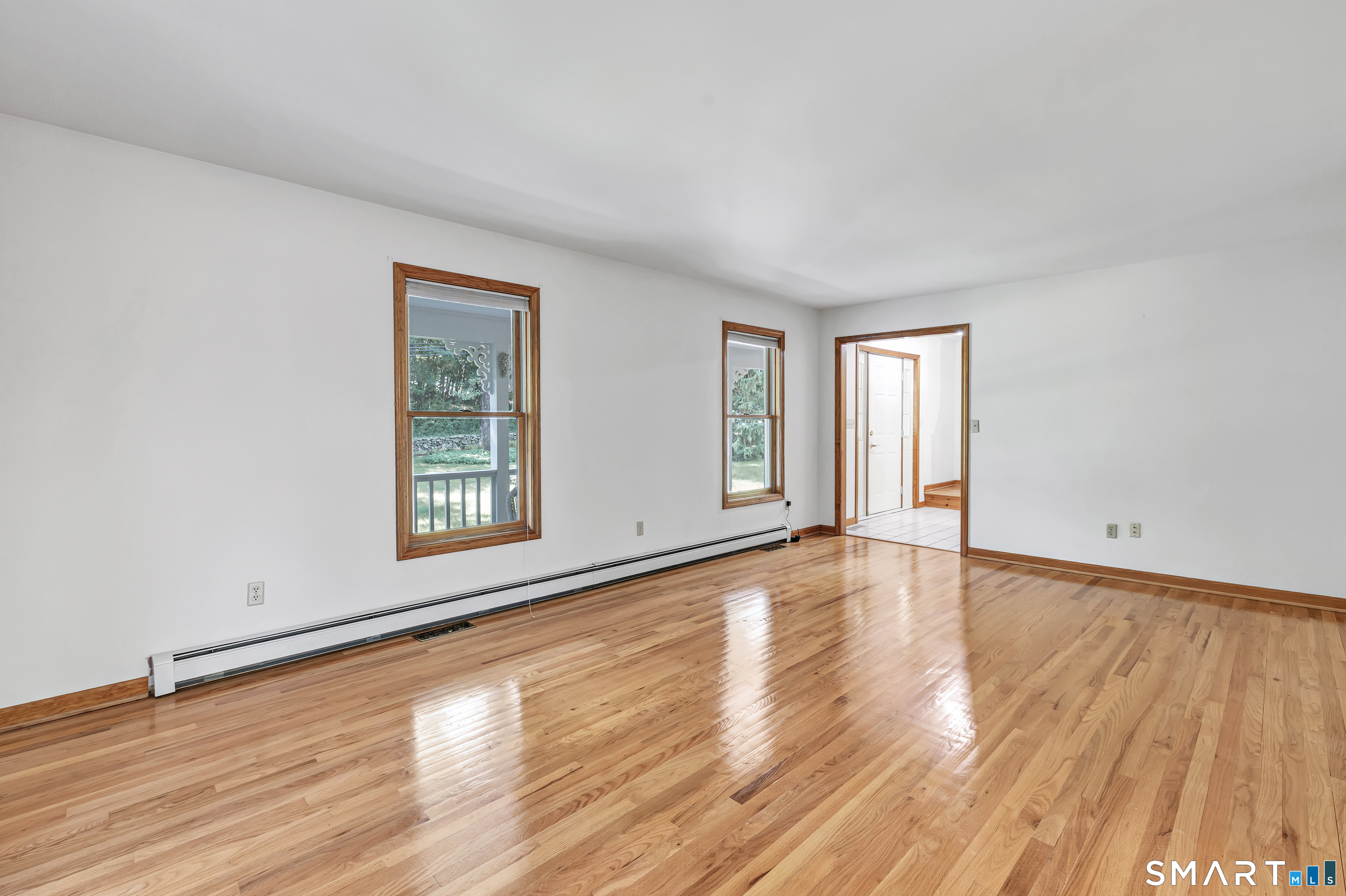 Vacant living room with polished hardwood floors, wood-trimmed windows, and a long baseboard heater.