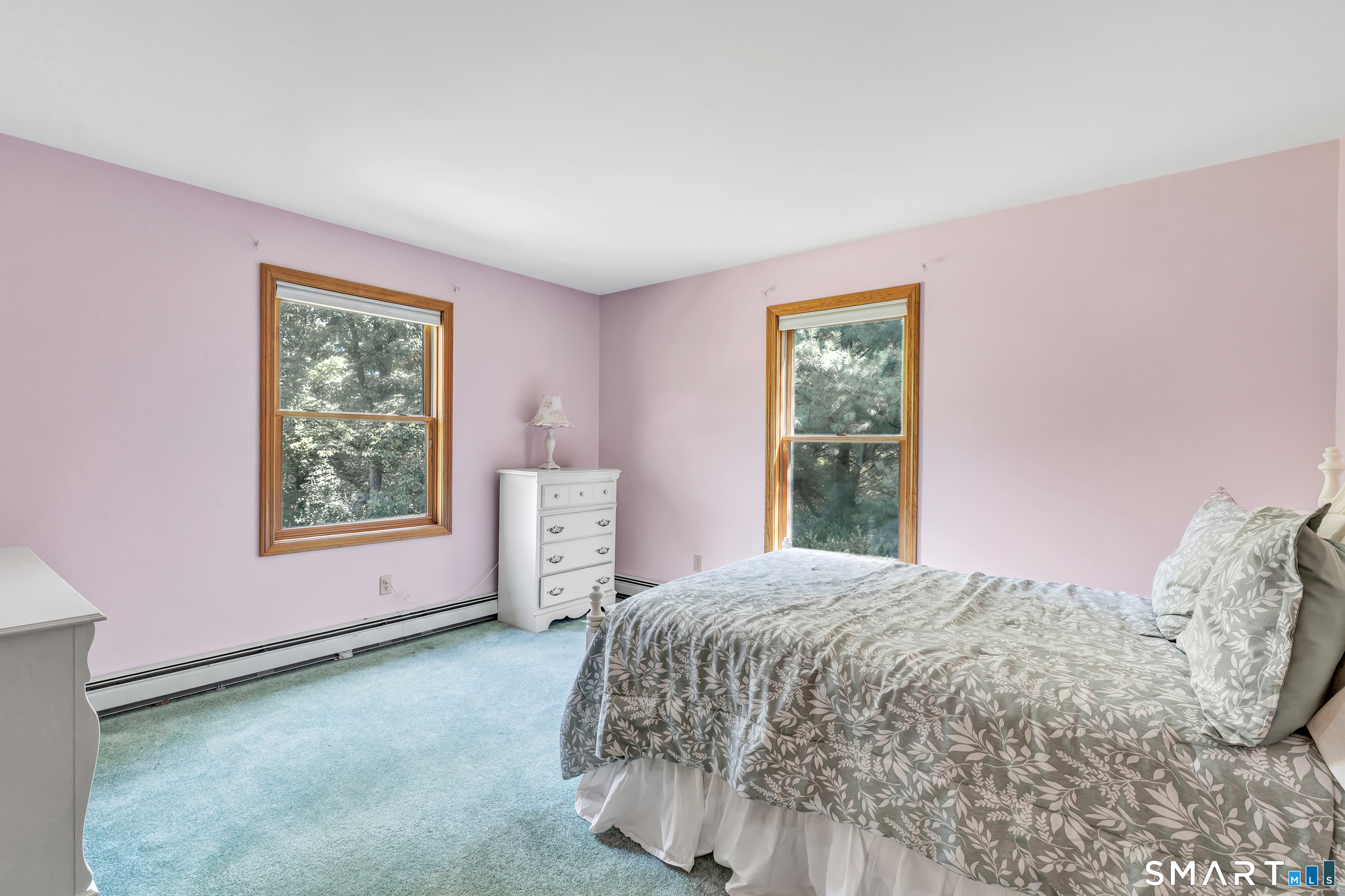 Bedroom with a gray leaf-patterned bedspread, pink walls, blue carpet, and two wood-trimmed windows.