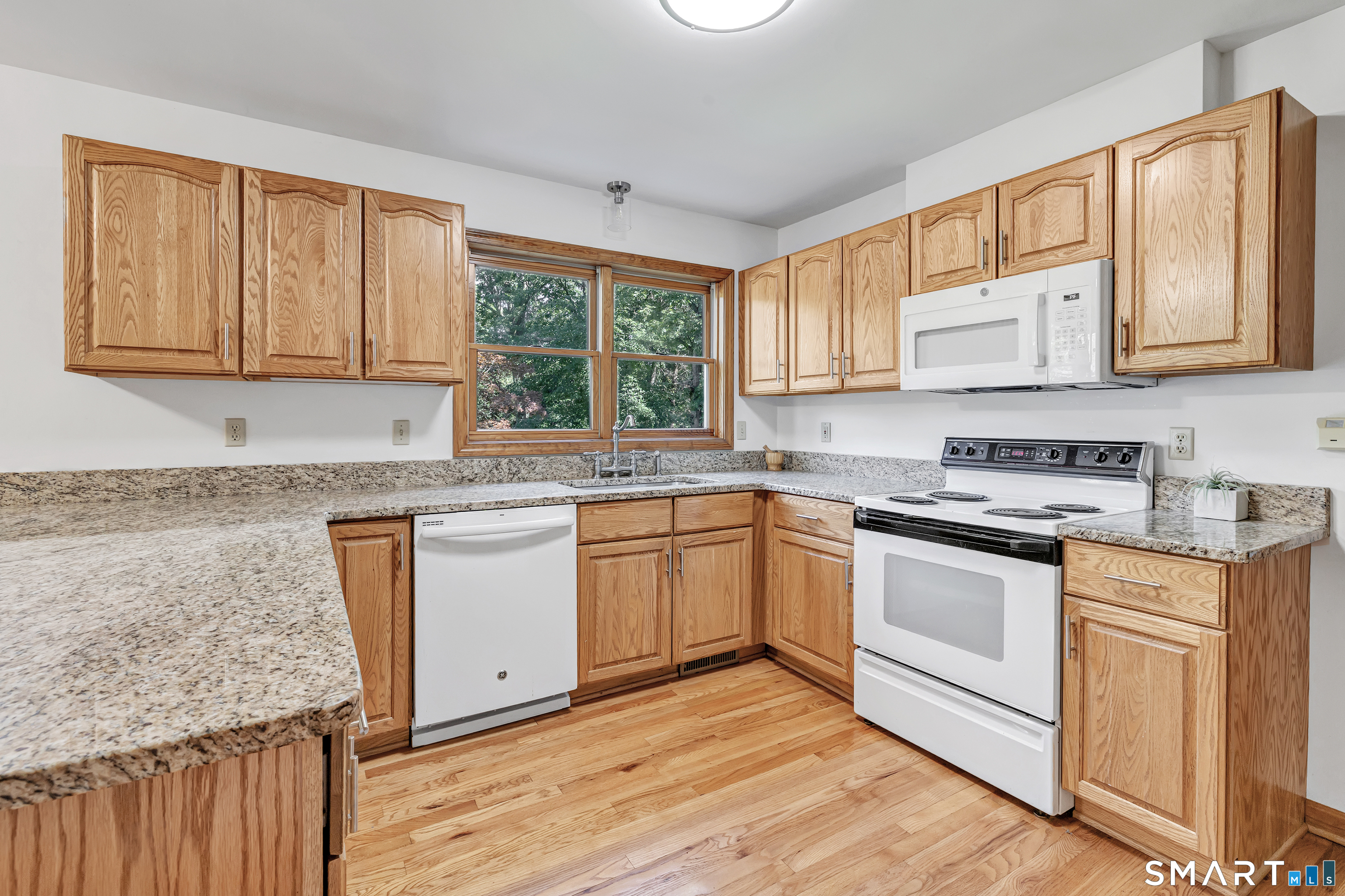 Kitchen with wood cabinets, granite counters, hardwood floors, and a window over the sink.