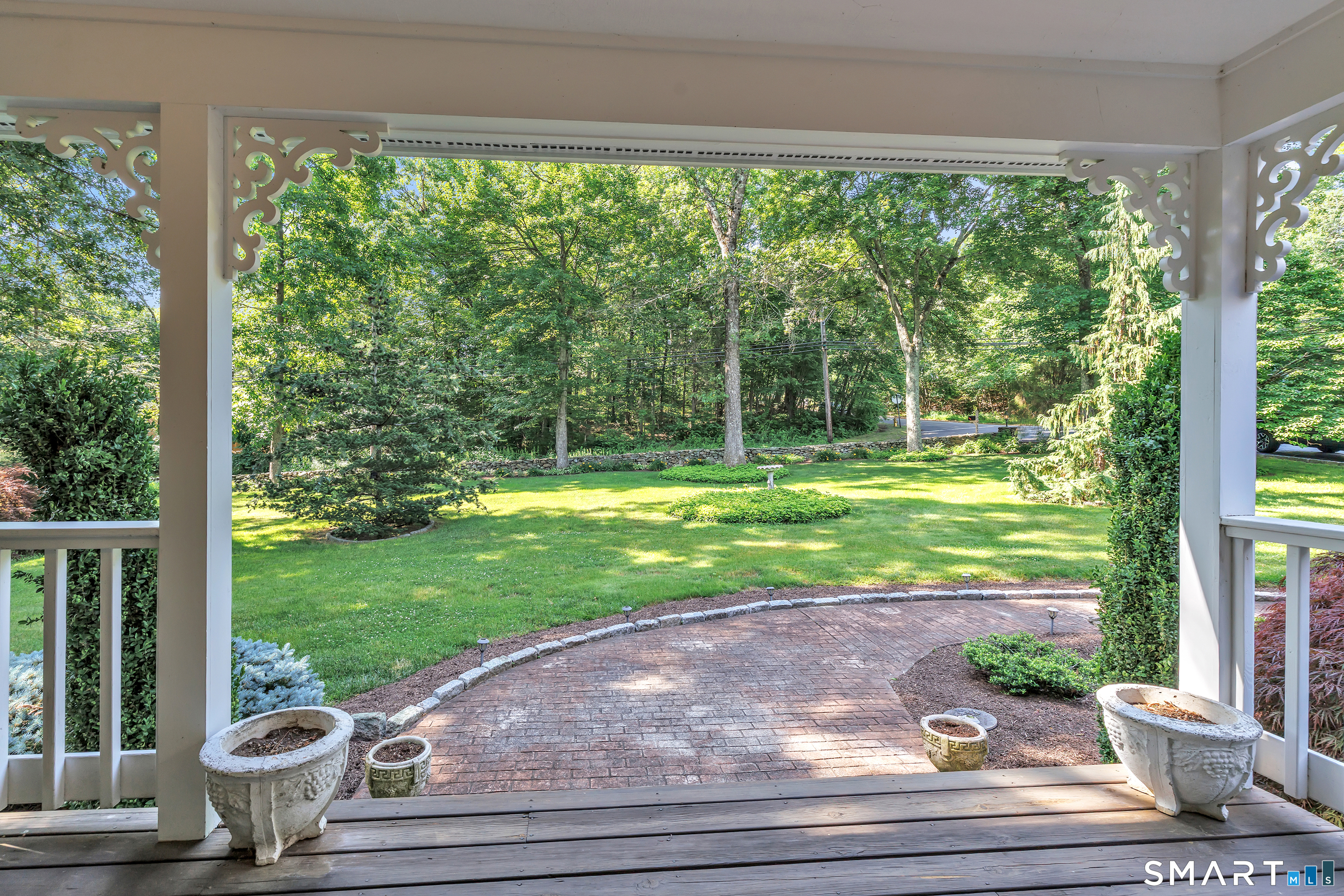 Covered porch overlooking a curved brick patio, landscaped lawn, and mature trees.
