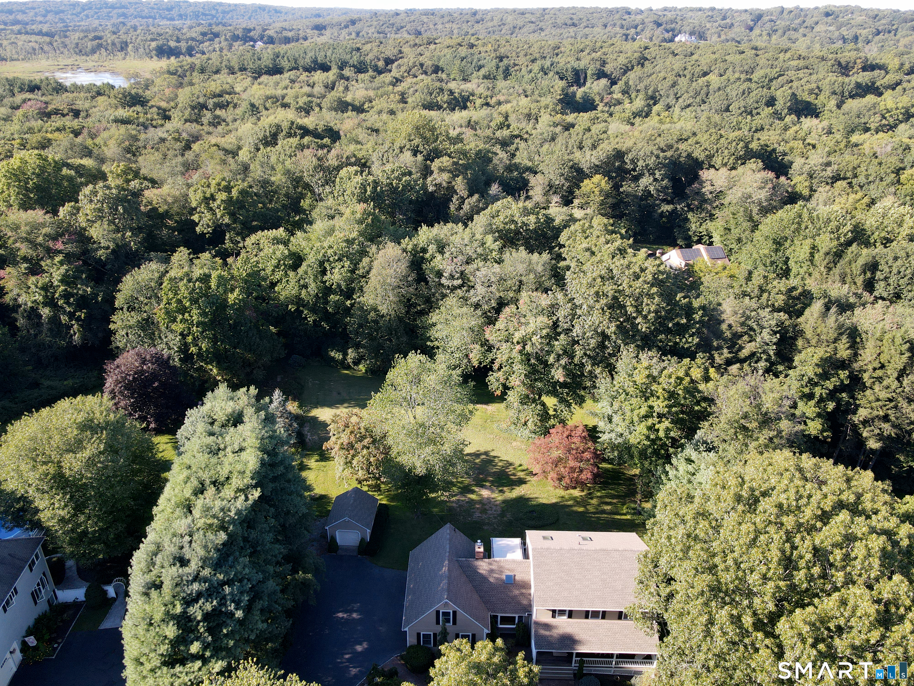 Aerial view of a home and outbuildings amid dense woodland, with a broad lawn.