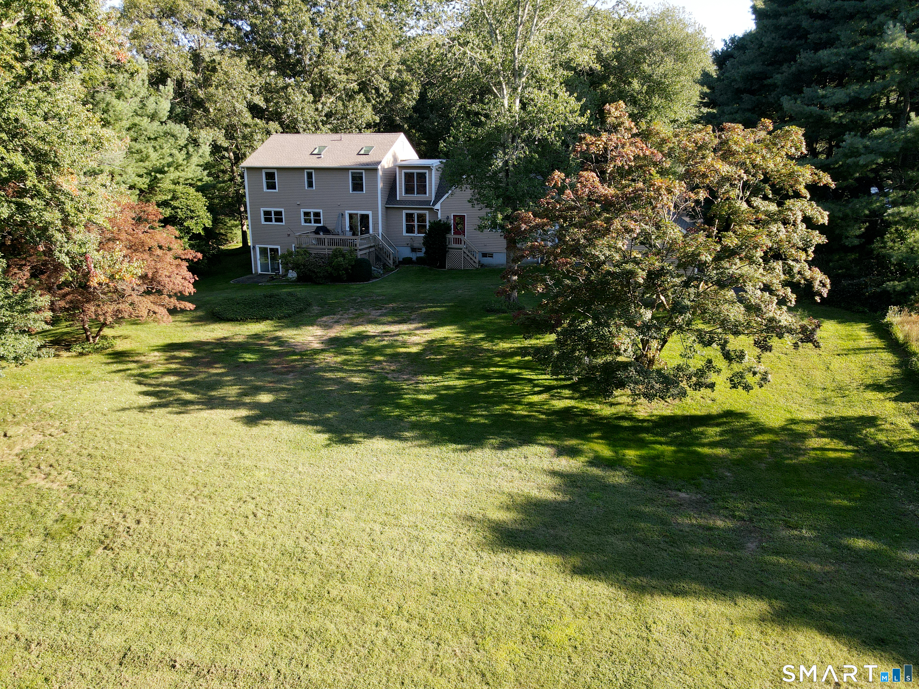 Rear of a two-story house with decks, mature trees, and a broad grassy lawn.