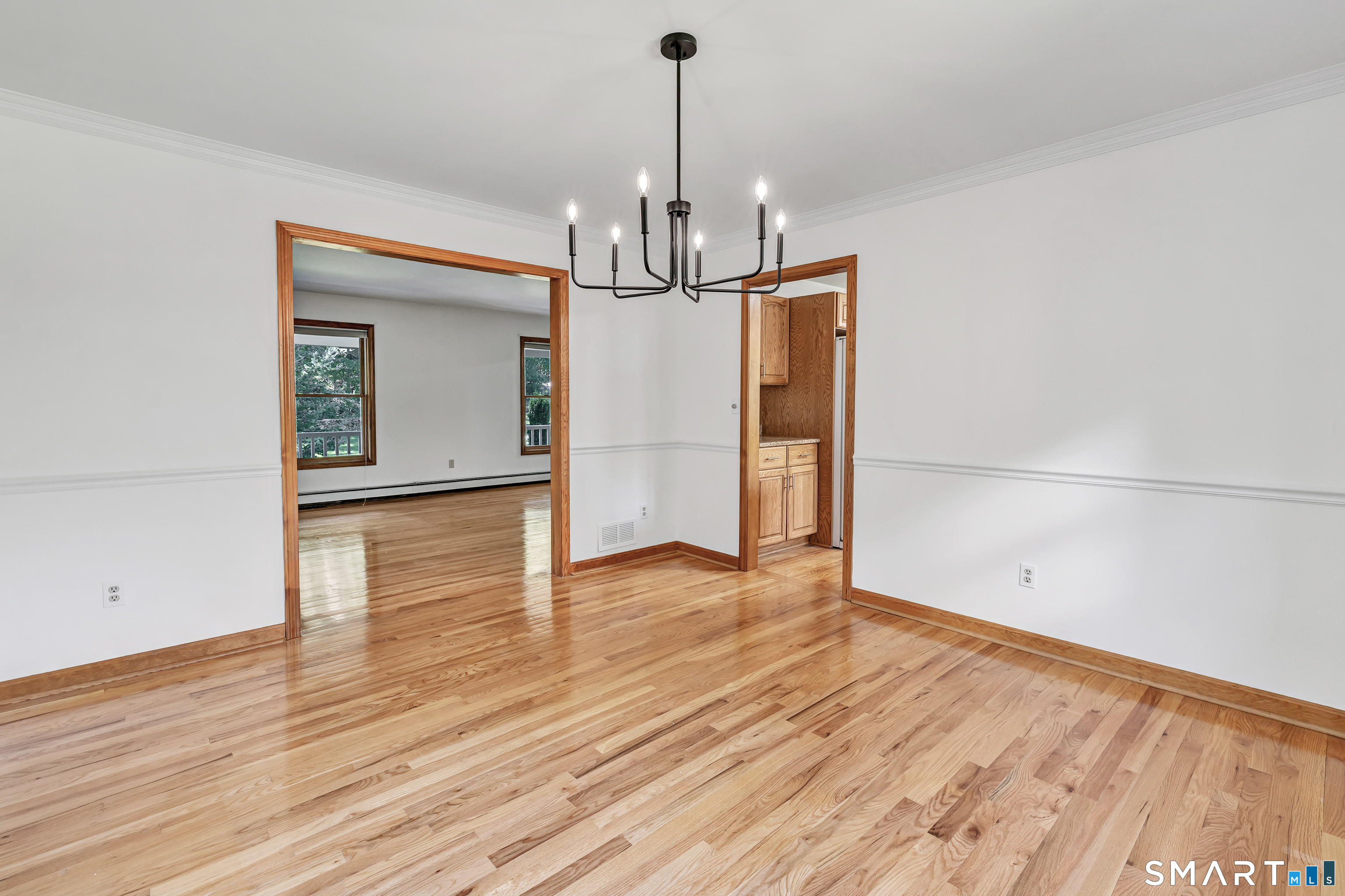 Empty dining room with polished hardwood floors, wood-trimmed openings, and a dark chandelier.