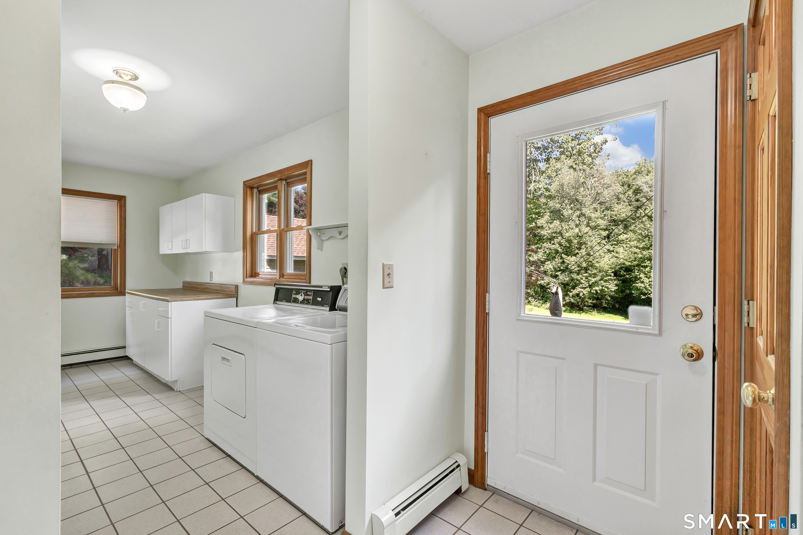 Laundry room with washer and dryer beside a windowed exterior door overlooking trees.