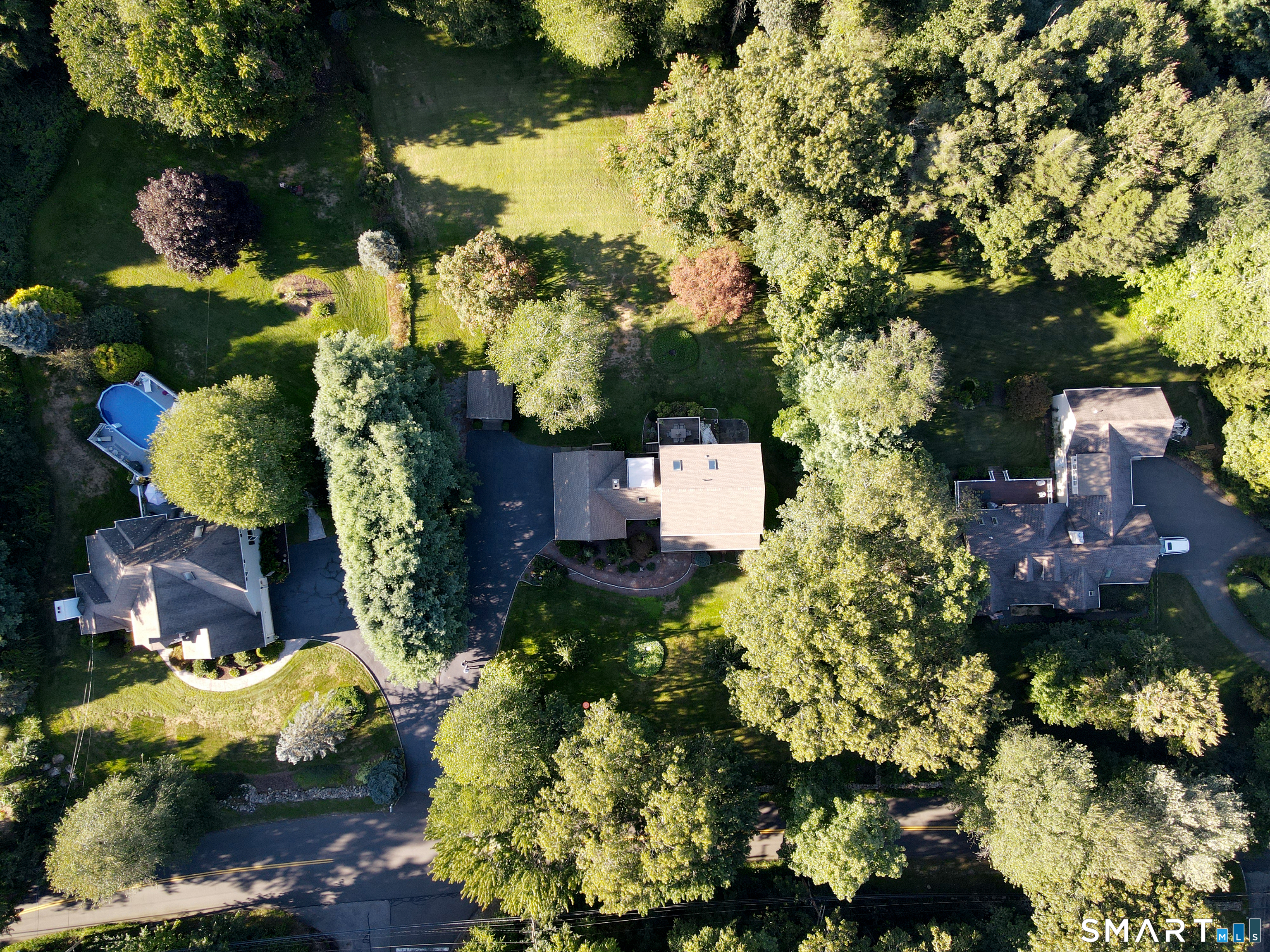 Aerial view of a tree-shaded home with a paved driveway and nearby swimming pool.