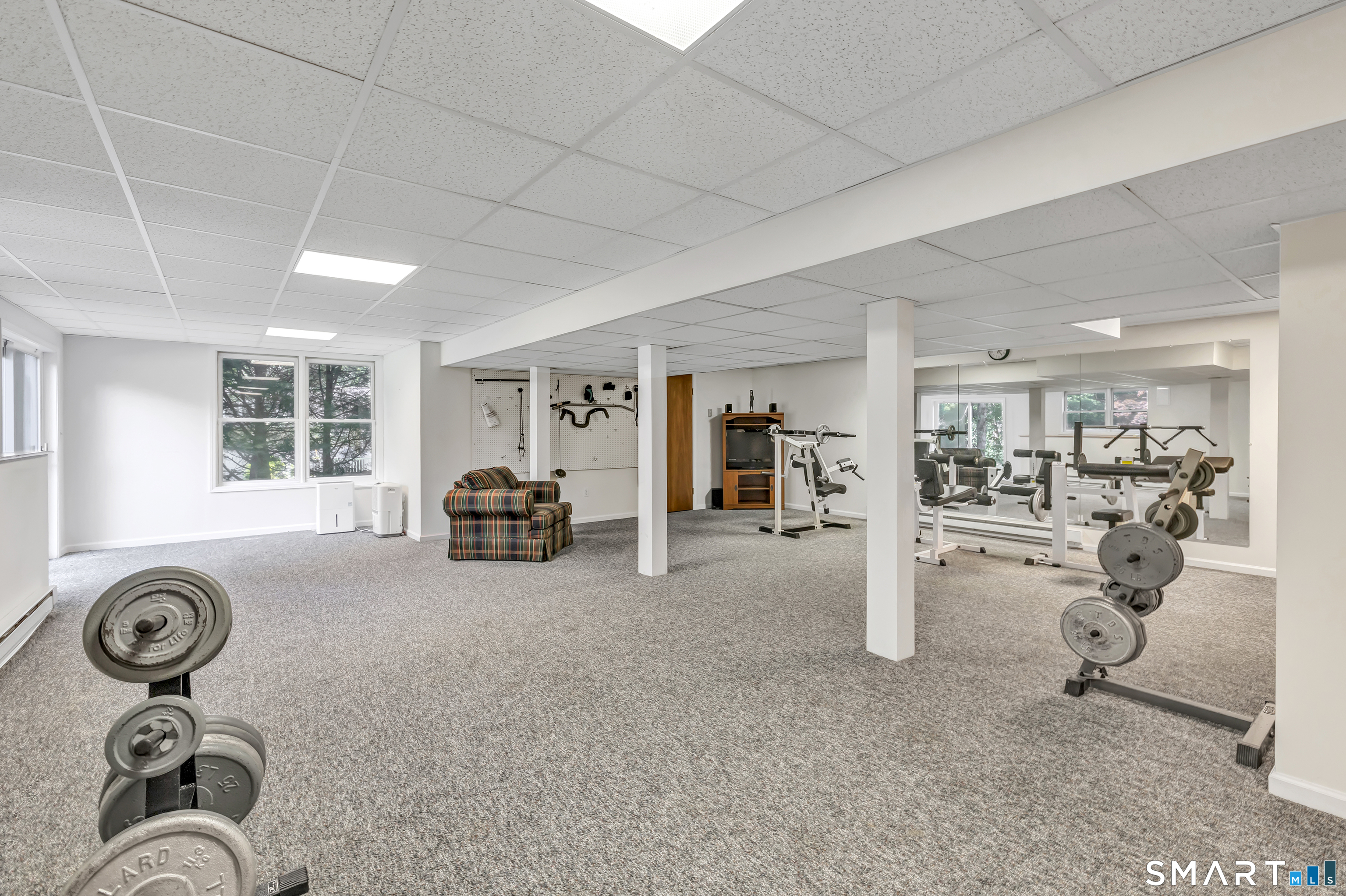 Home gym with weight machines, free weights, mirrored wall, and plaid armchair.