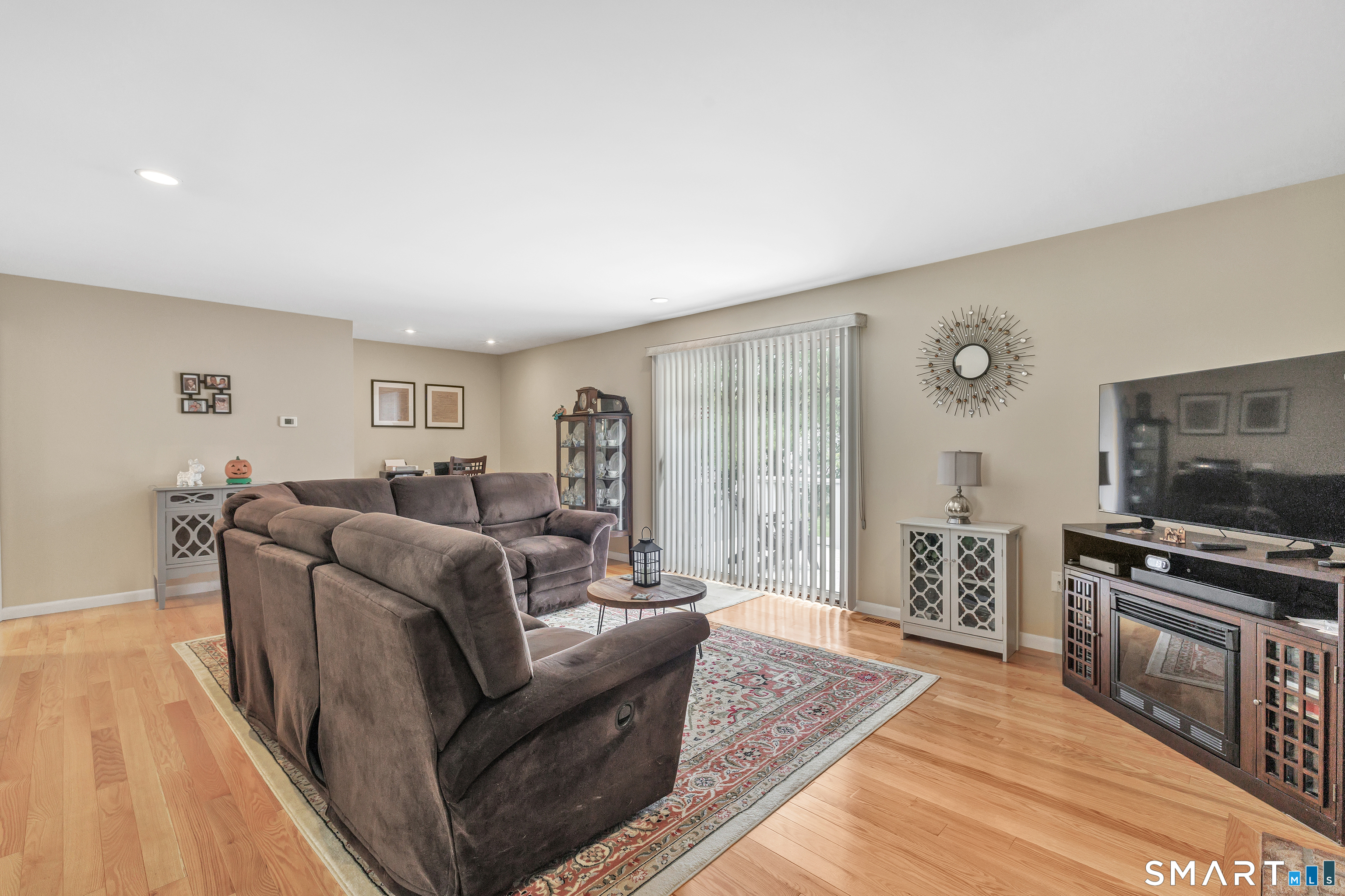 Living room with a dark sectional, patterned rug, hardwood floors, and sliding glass door.