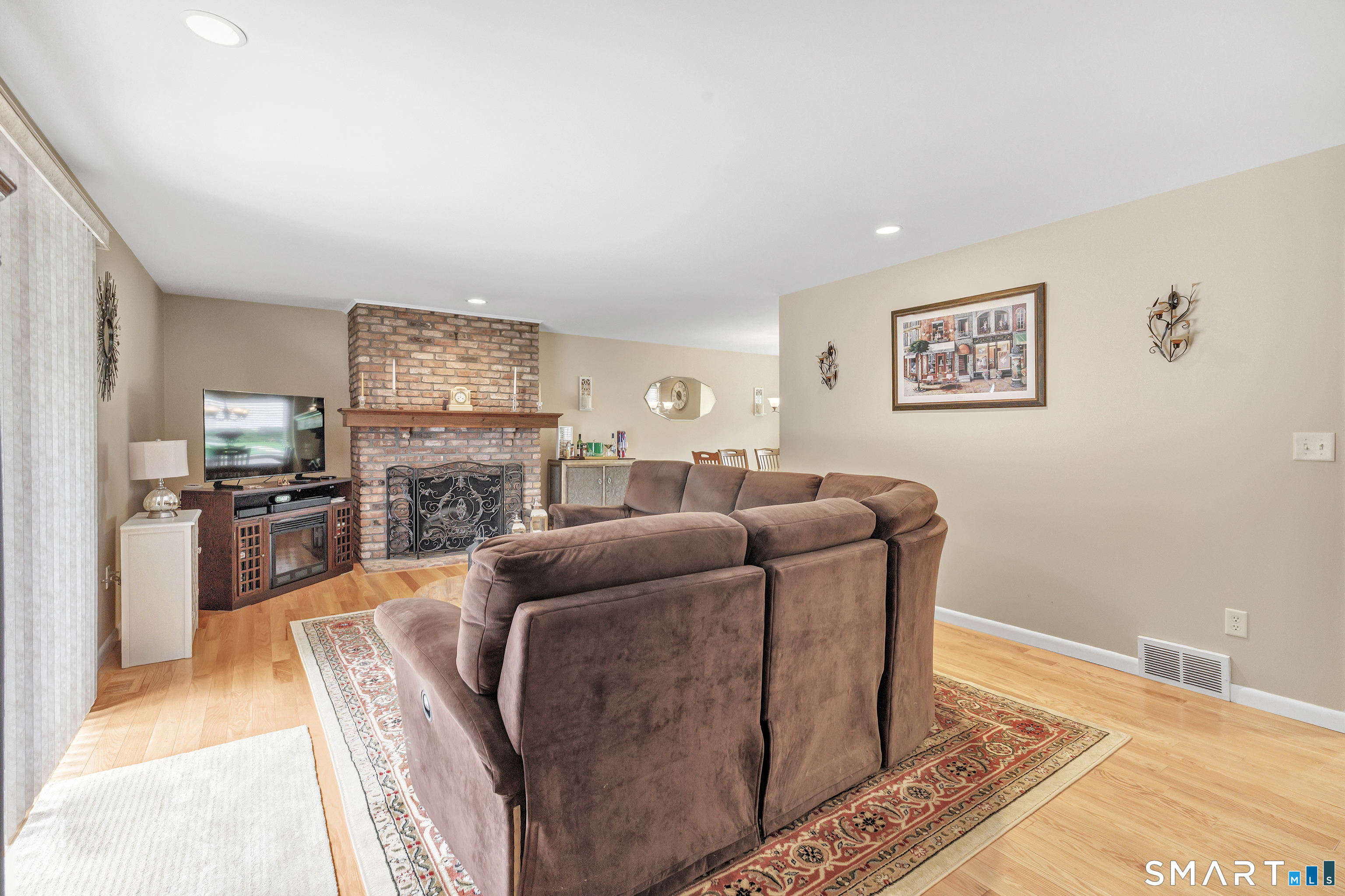 Living room with a brown sectional, brick fireplace, television, and hardwood floors.