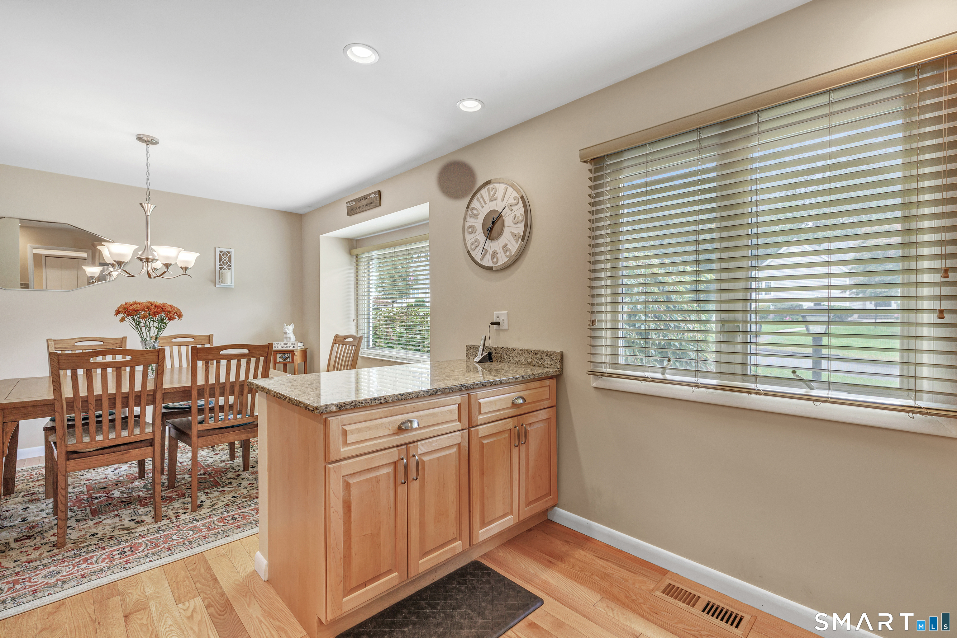 Kitchen and dining area with a granite-topped island, wooden dining set, and large windows with blinds.