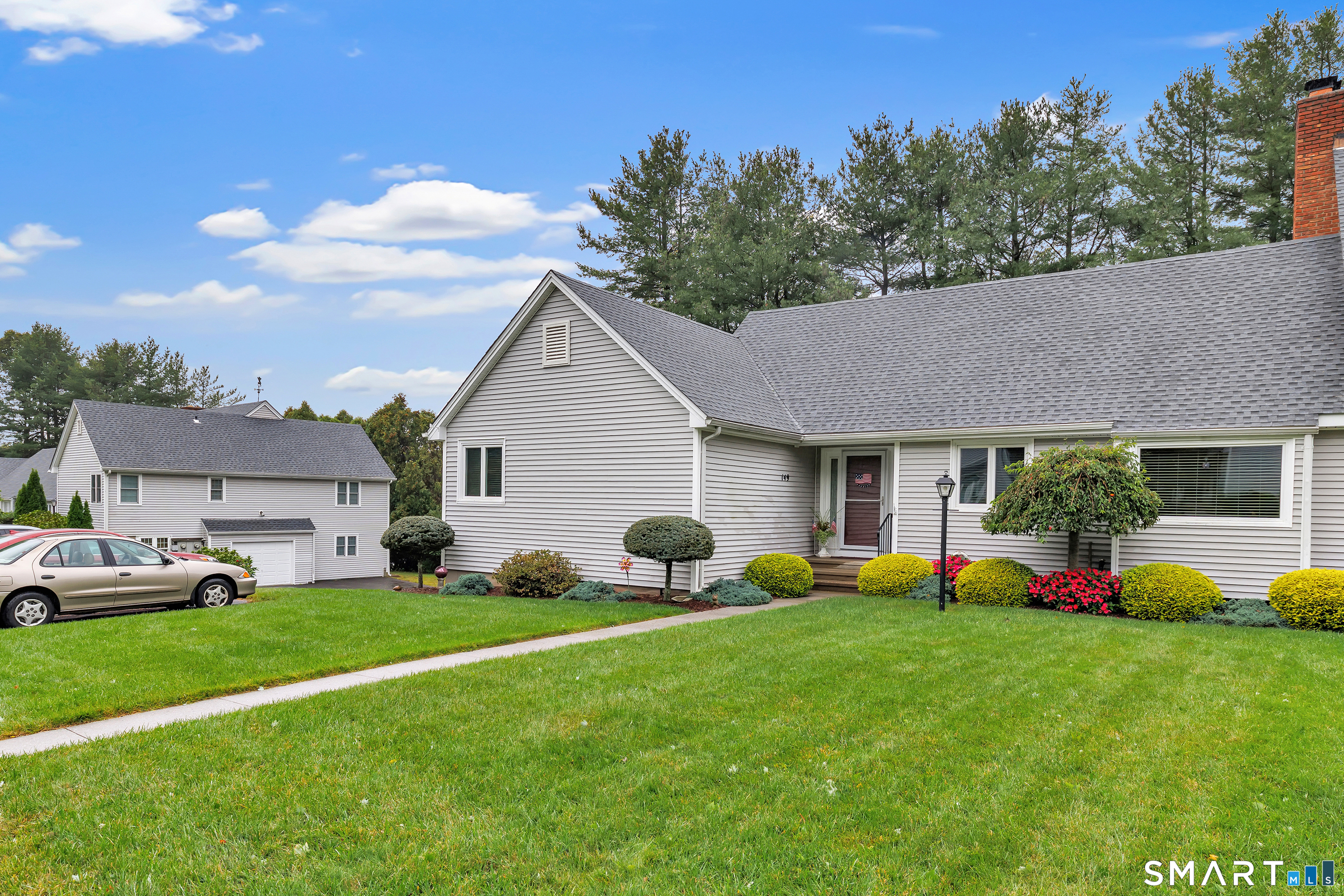 Gray-sided home with landscaped front lawn, flowering shrubs, and a walkway.