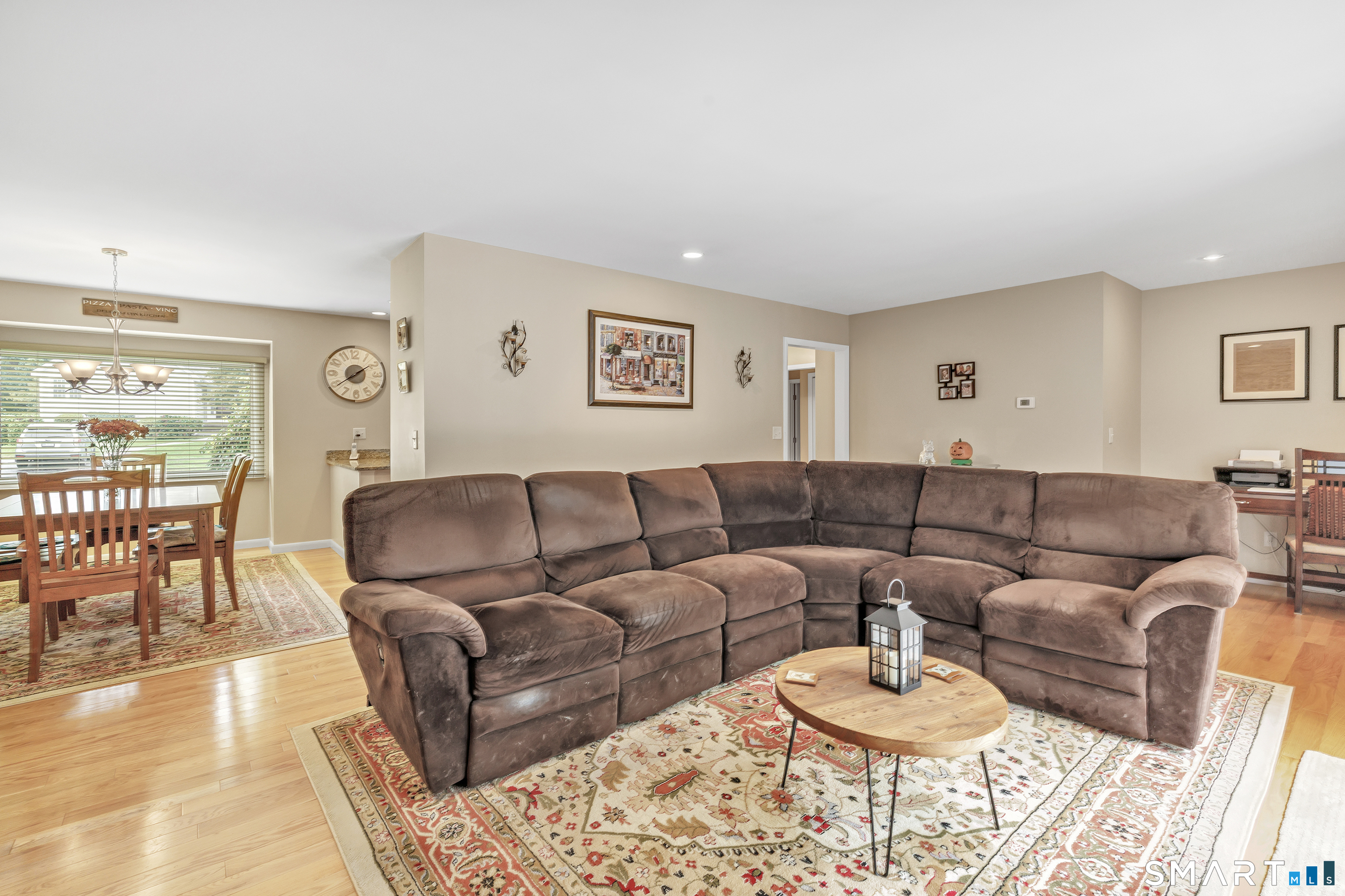Living room with a large brown sectional, round coffee table, patterned rug, and adjoining dining area.