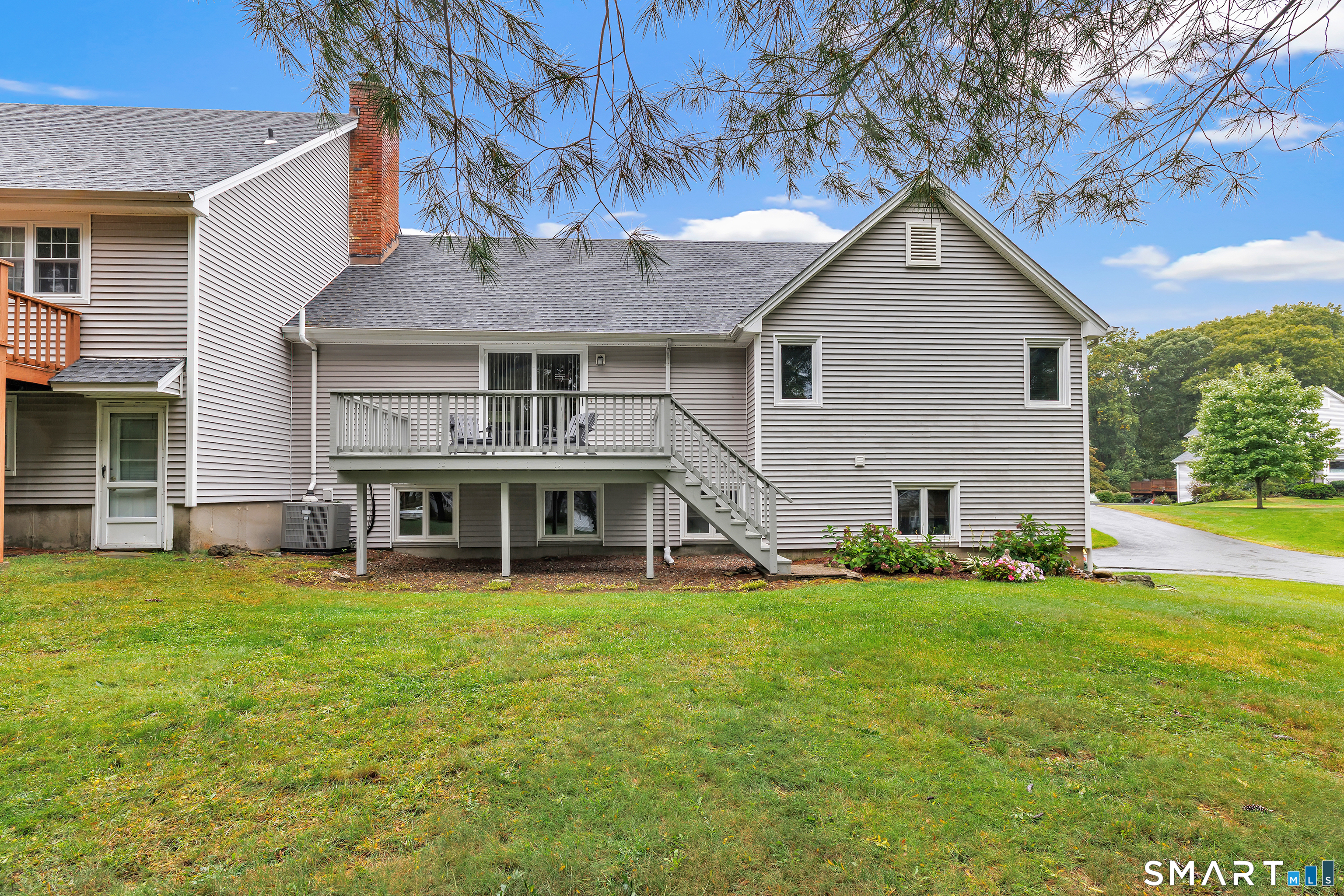Rear of gray-sided home with a raised deck and stairs overlooking a broad lawn.