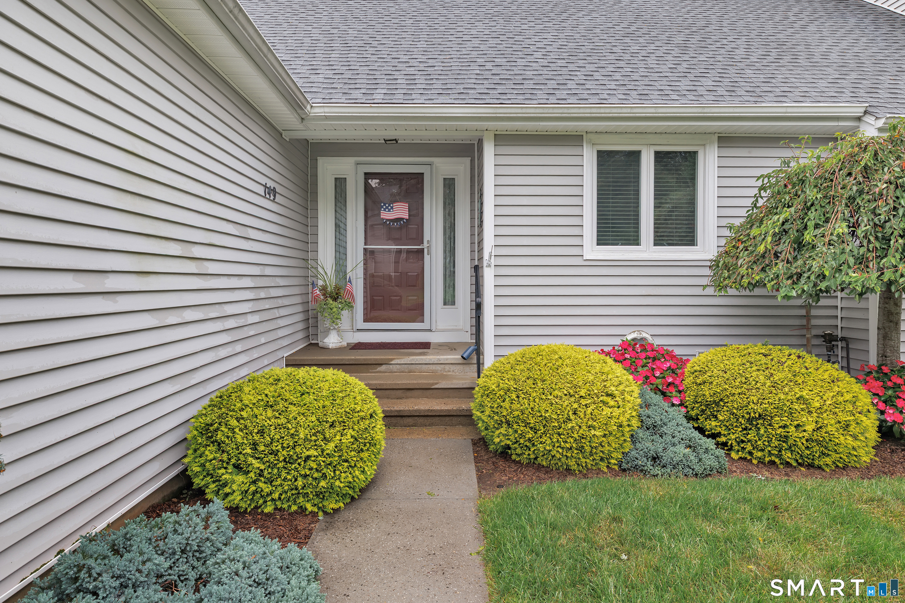 Home entrance with gray siding, concrete steps, and colorful landscaping.