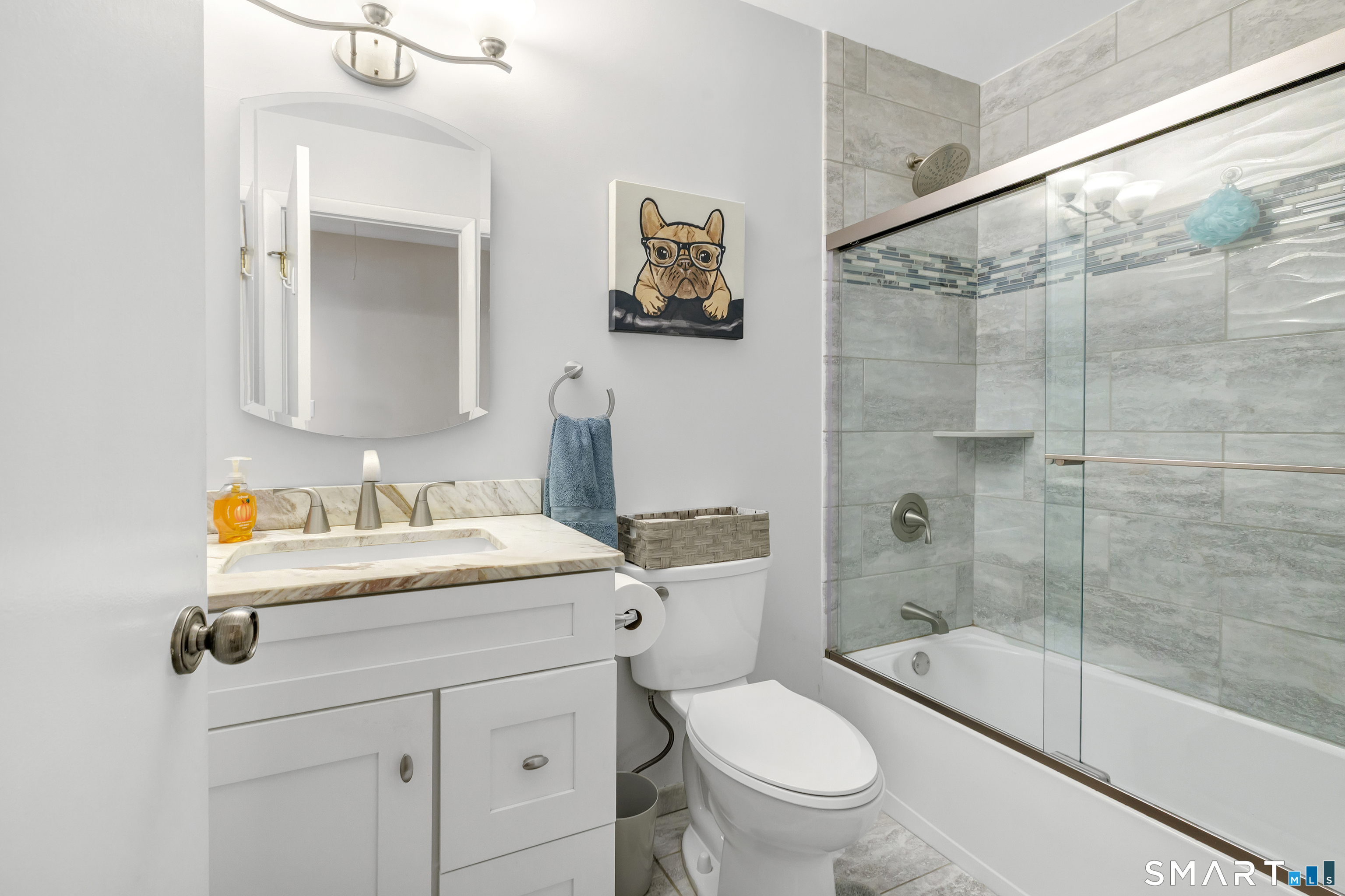Bathroom with a white vanity, toilet, and glass-enclosed tub and shower with gray tile.