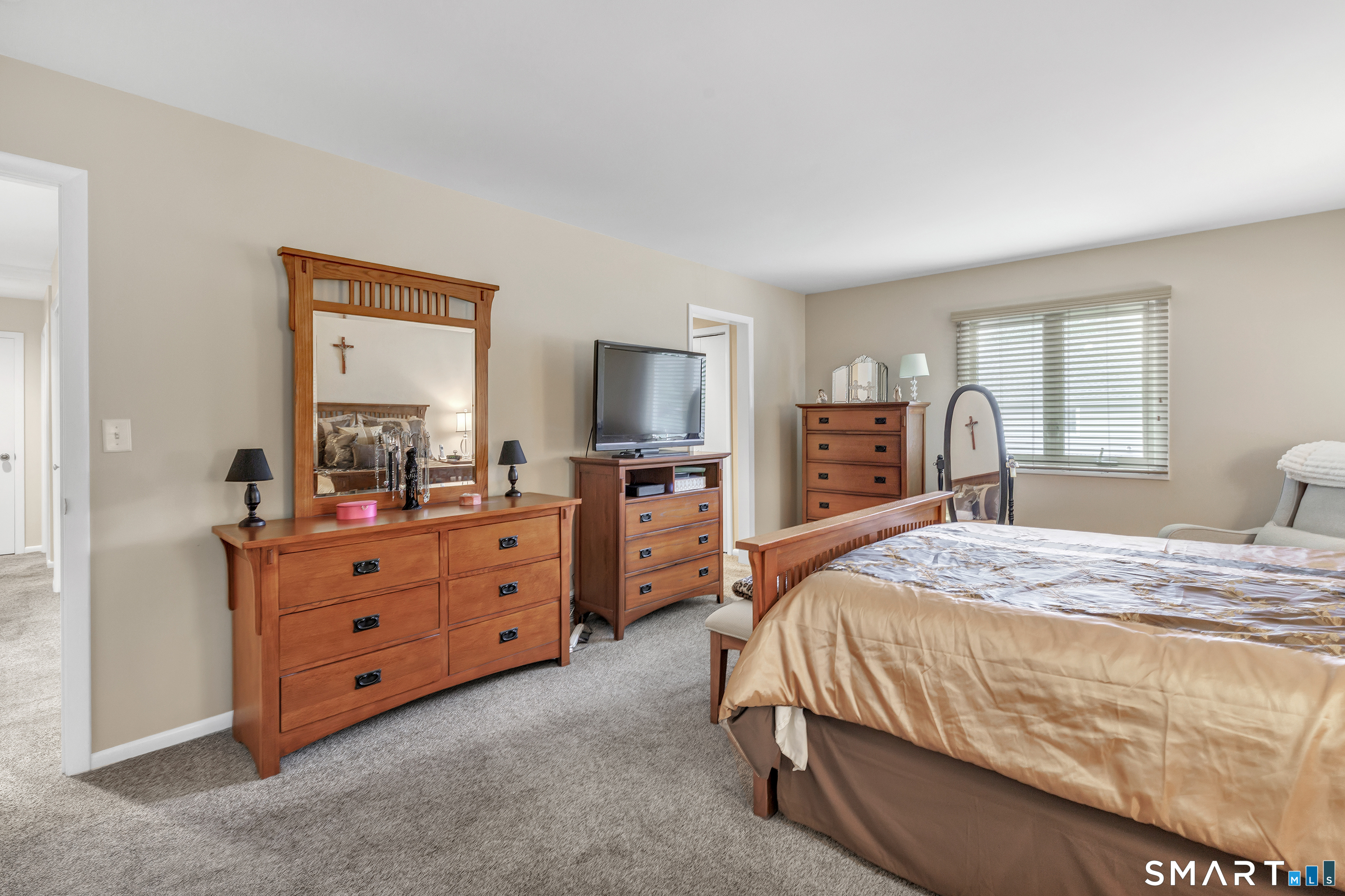 Bedroom with a wooden bed and matching dressers, carpeted floor, and large window with blinds.