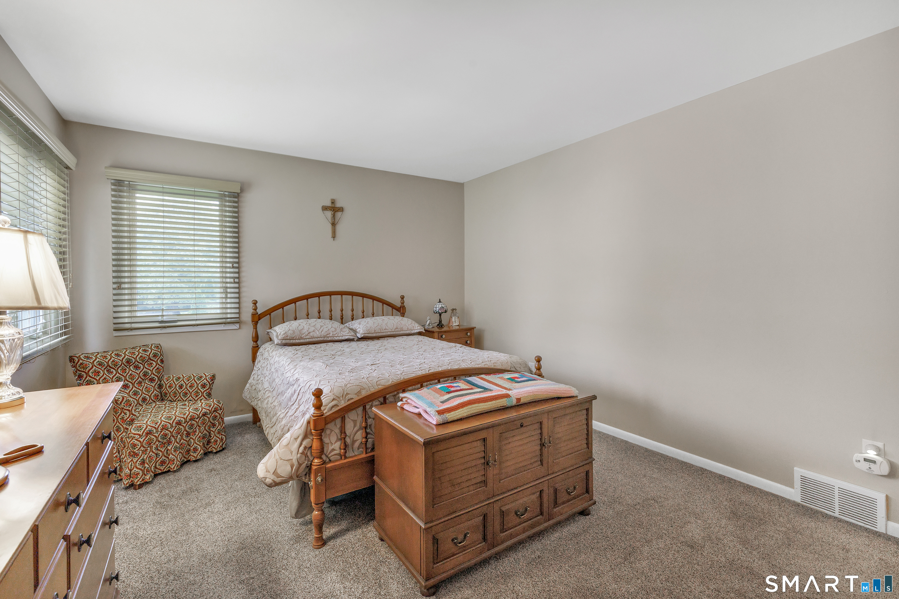 Furnished bedroom with a wooden bed, patterned armchair, and matching wooden furniture.