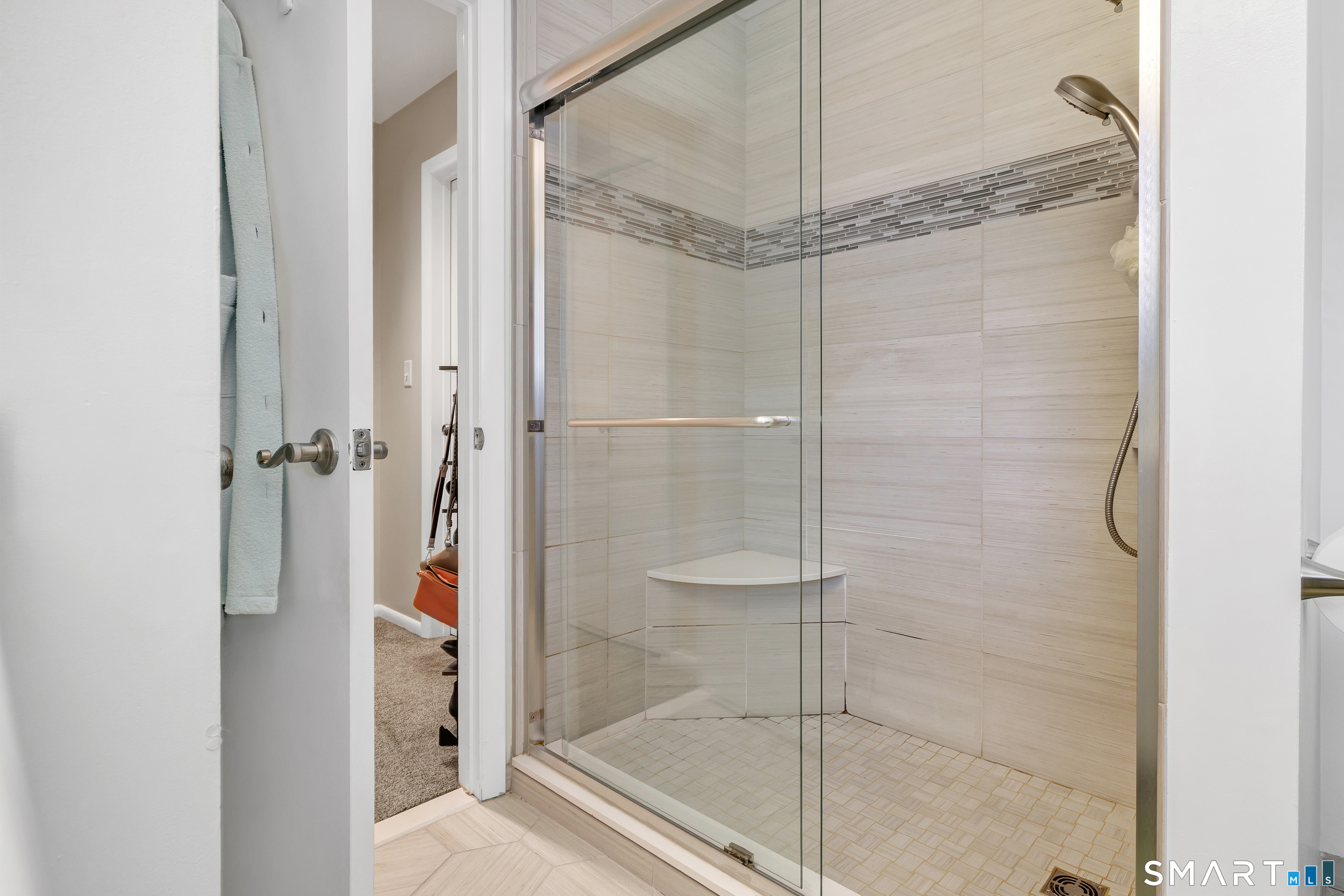 Walk-in shower with clear glass doors, tiled walls, a corner seat, and mosaic accent strip.
