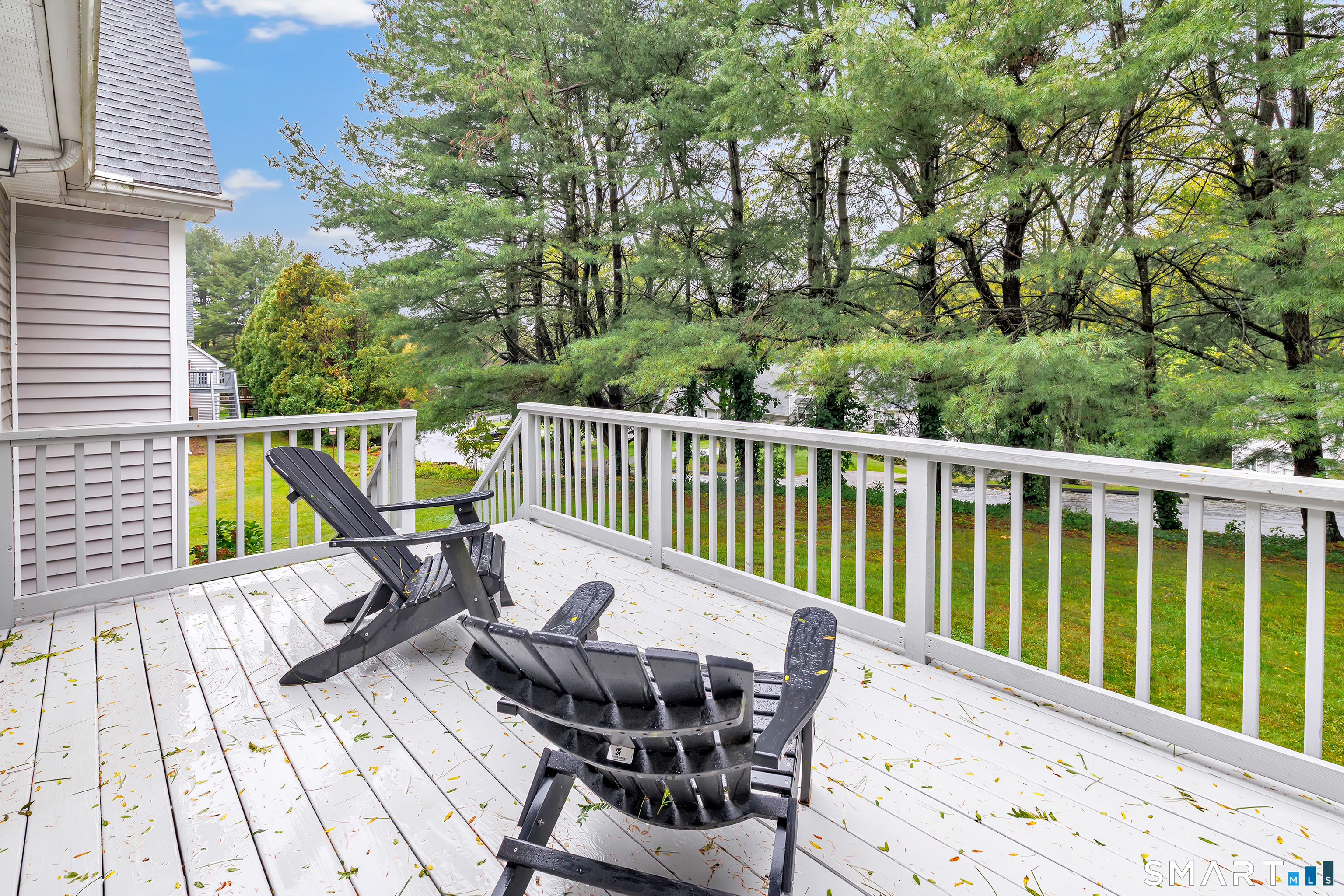 White deck with black Adirondack chairs overlooking a leafy wooded yard.