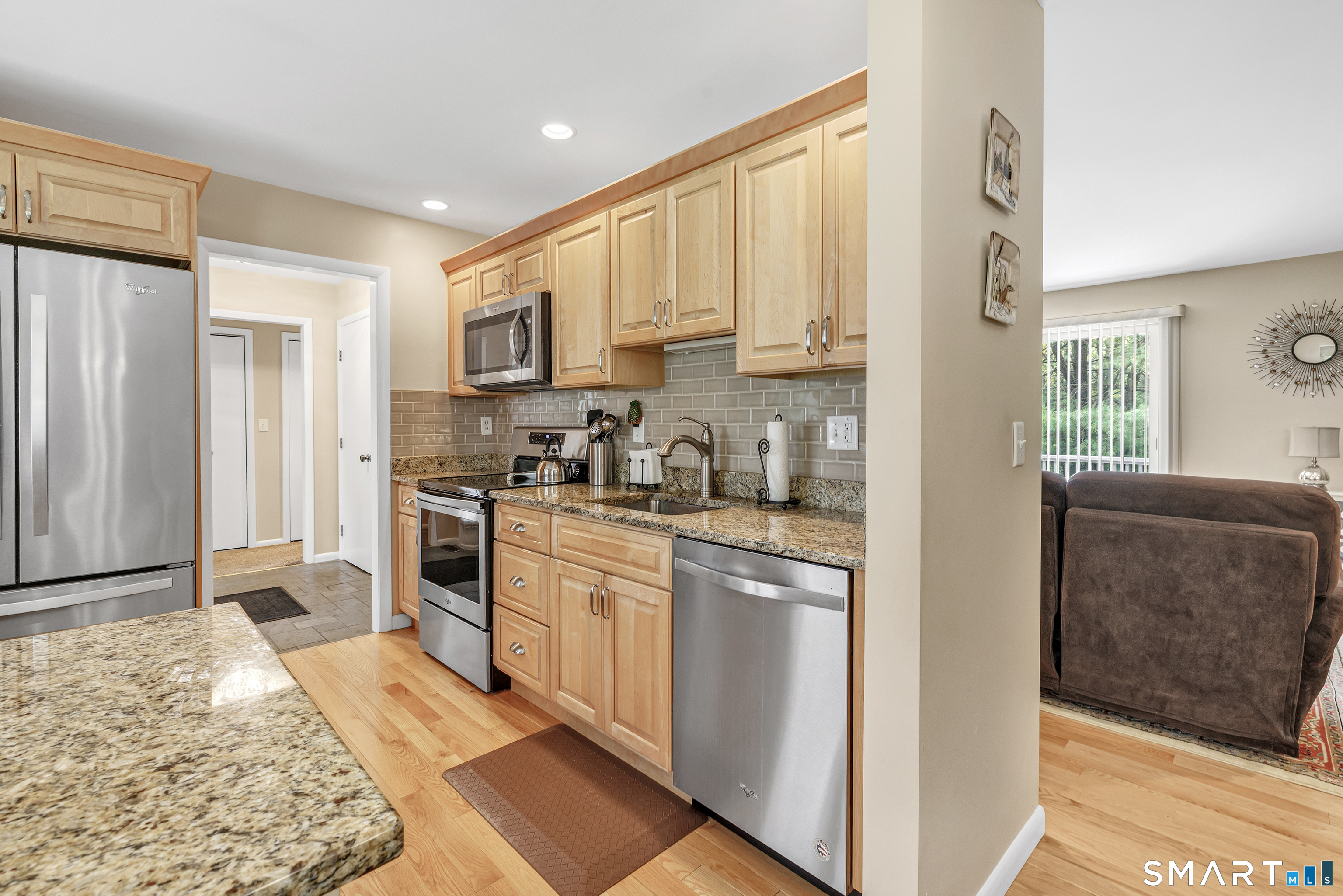 Kitchen with light wood cabinets, granite counters, stainless steel appliances, and a view into the living room.
