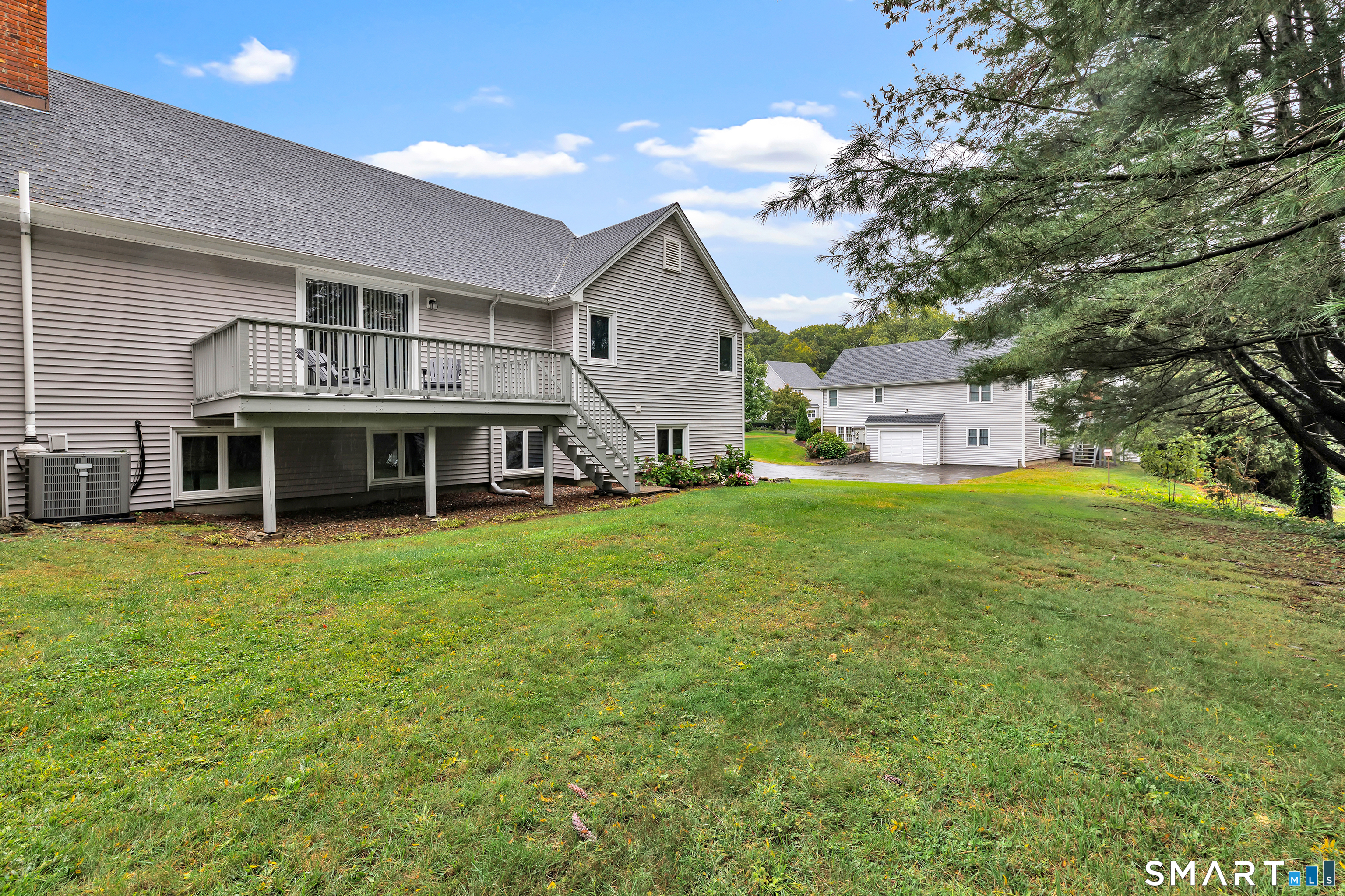 Home’s rear exterior with a raised deck and stairs overlooking a broad lawn and neighboring garage.