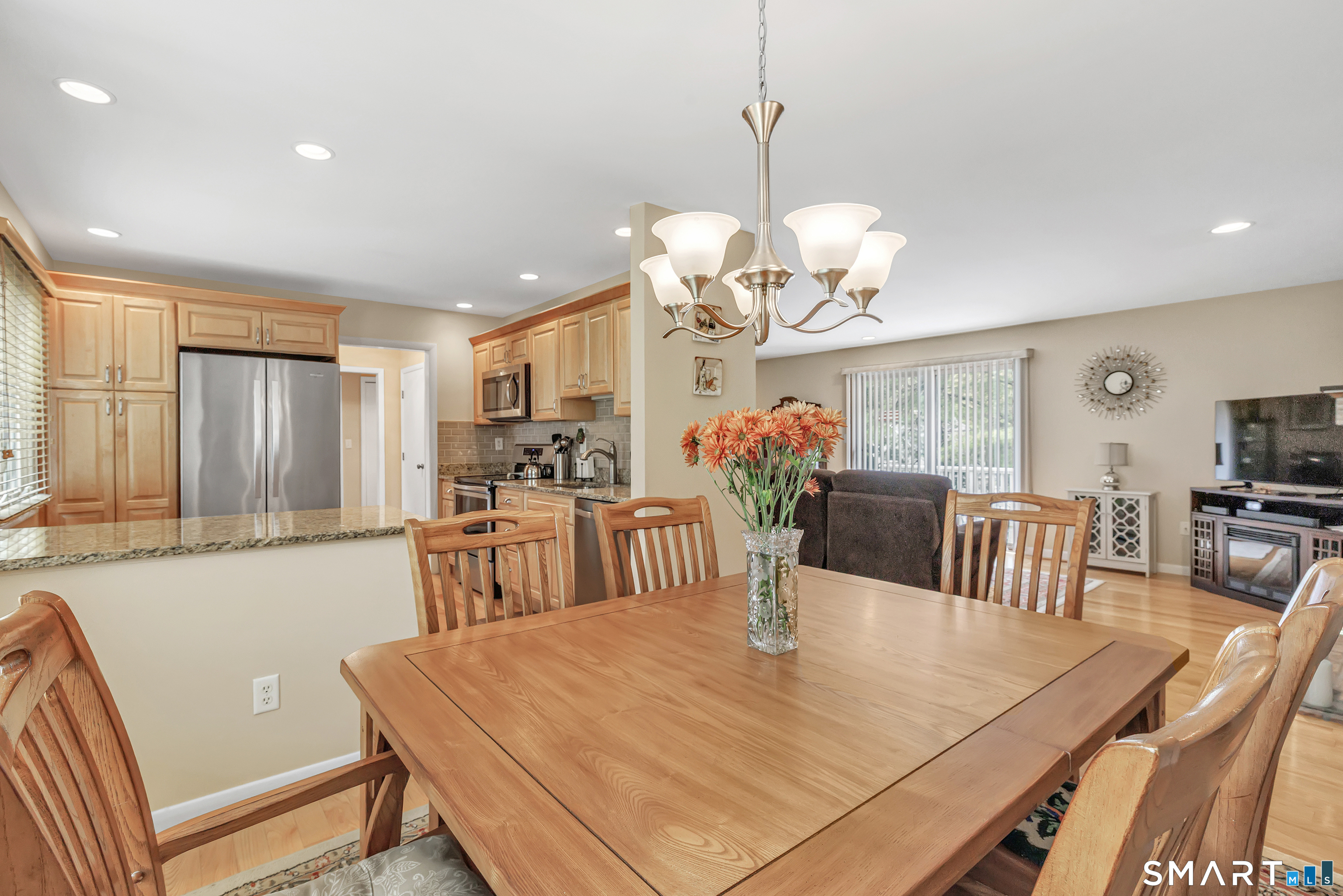 Open-plan dining area with a large wooden table beside a light-wood kitchen and living room.