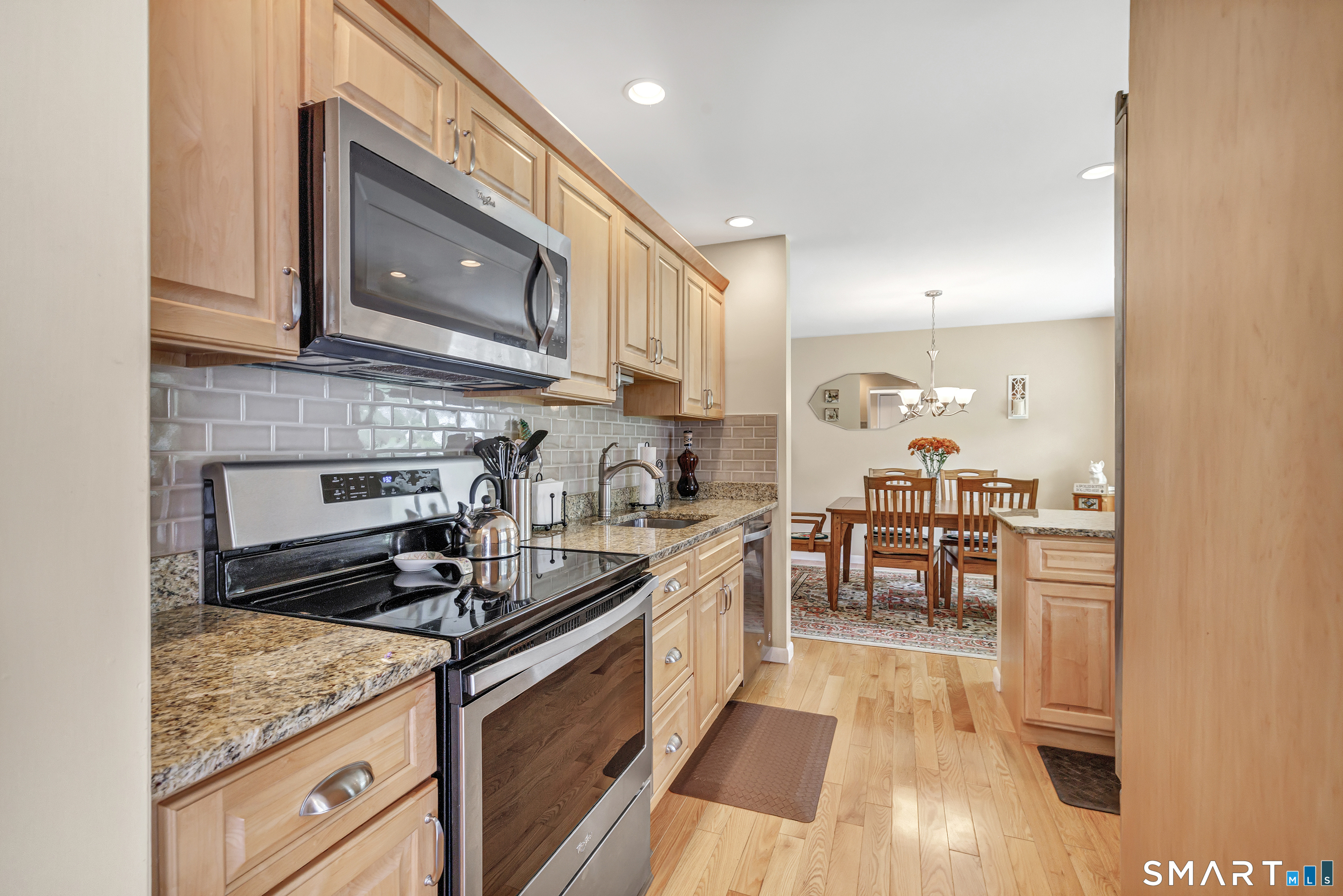 Kitchen with light wood cabinets and granite counters opening to a dining area with a wooden table.