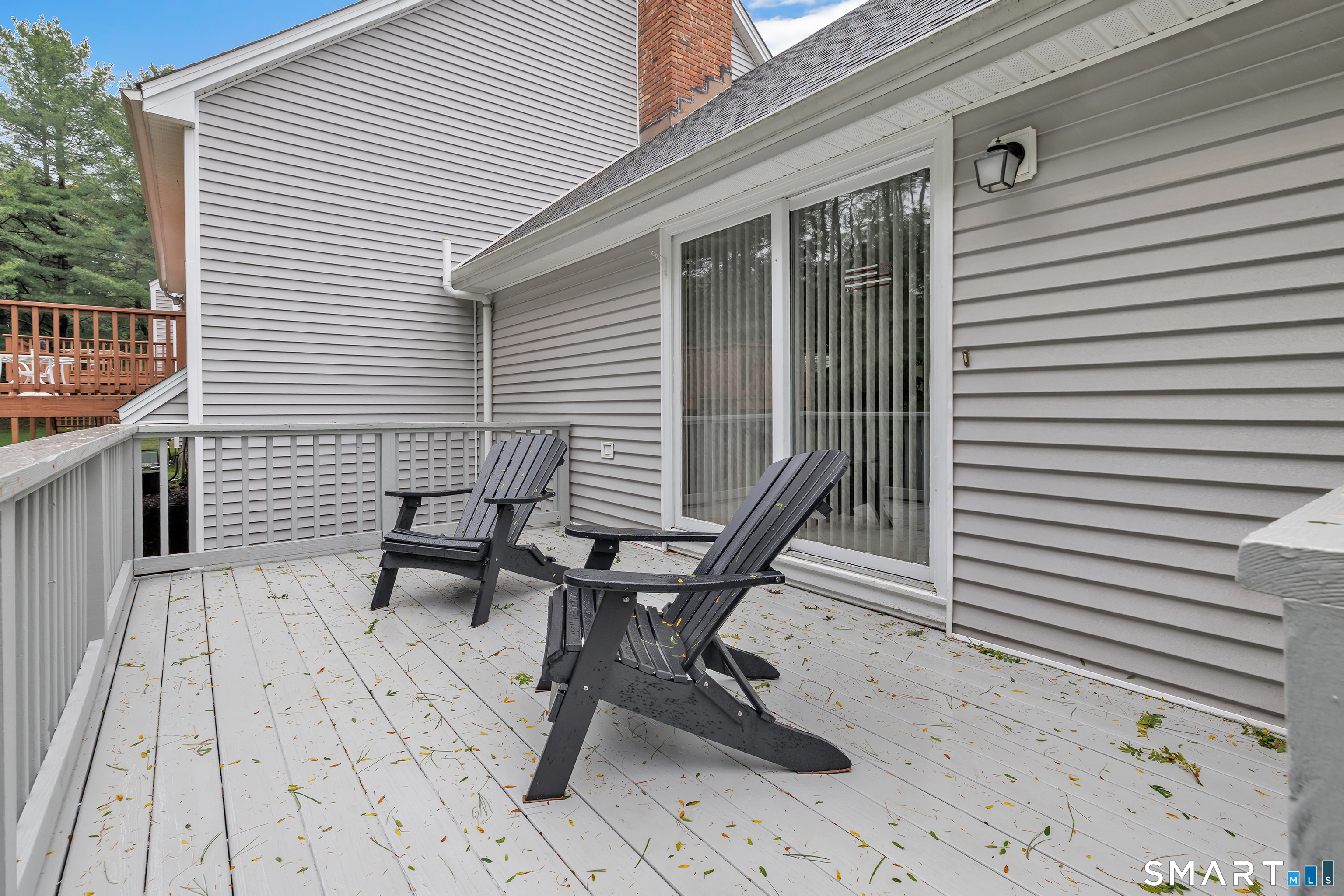 White deck with two dark Adirondack chairs beside a gray-sided home and sliding glass door.